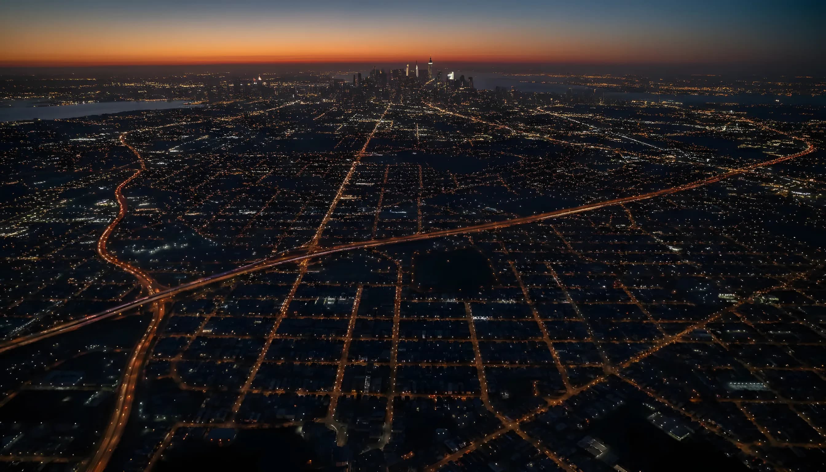 Aerial view of Long Island suburbs at dusk, with city lights stretching towards the distant New York City skyline.