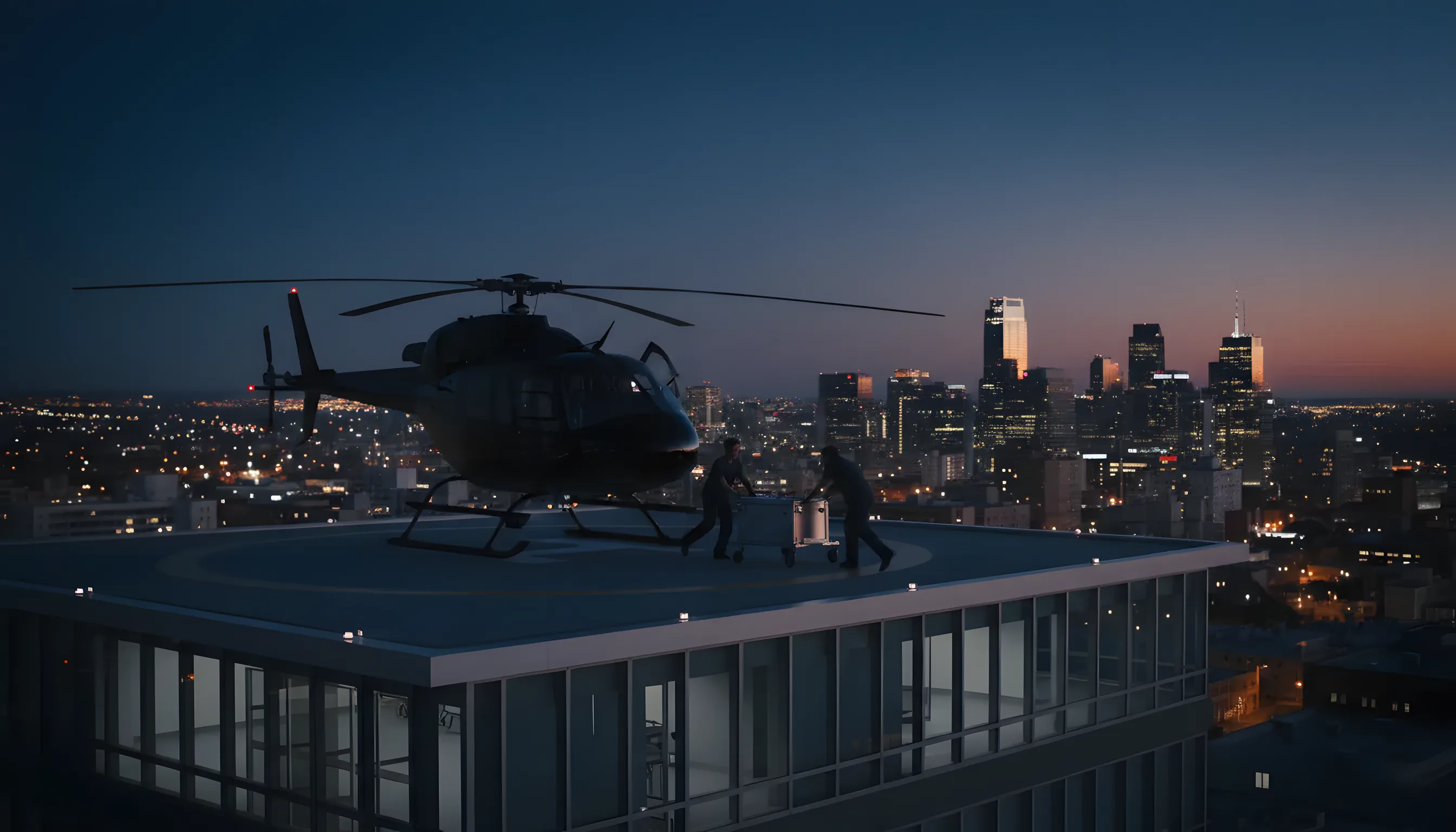 A helicopter on a hospital rooftop helipad at dusk, prepared for a medical transport flight over a city.