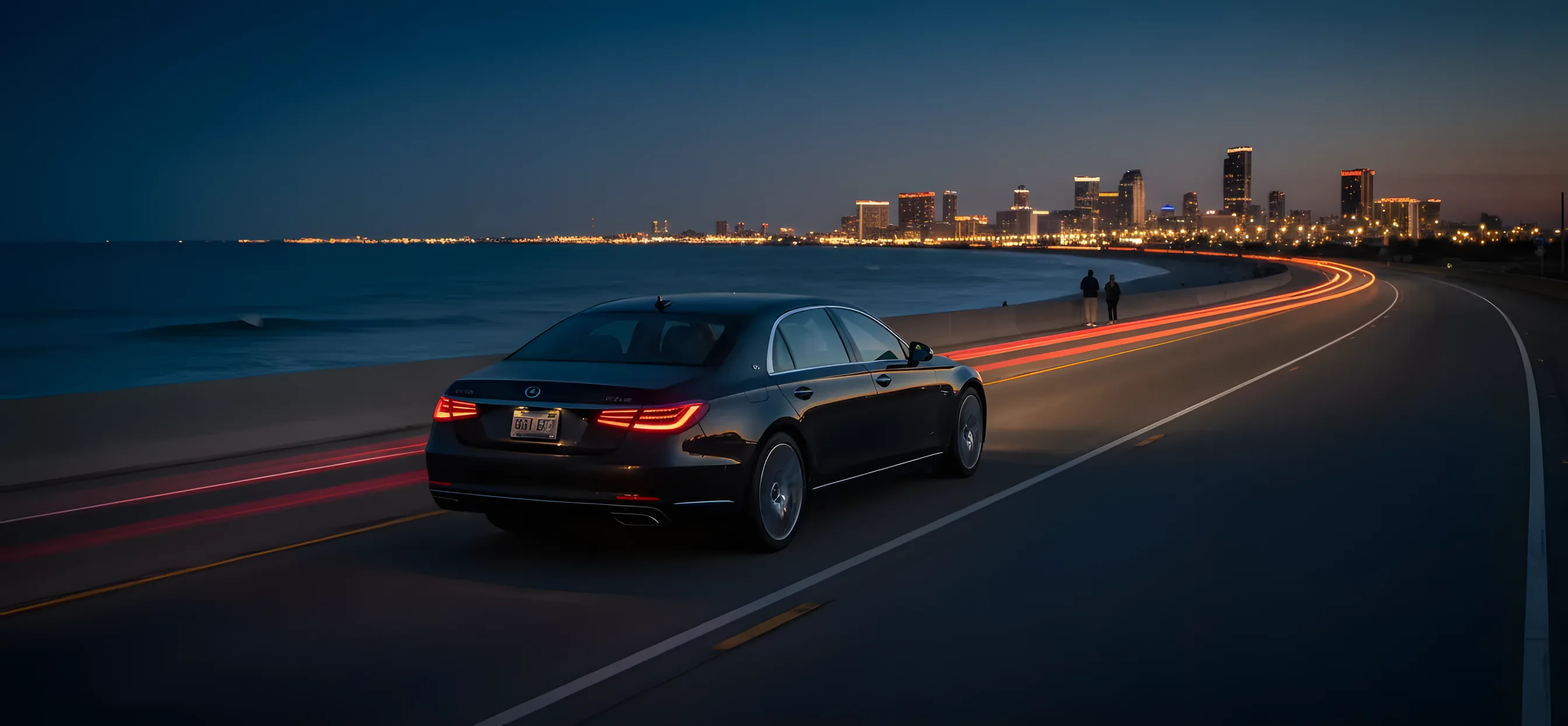 A dark car speeds along a coastal highway at twilight, with the lights of a distant city visible on the horizon.