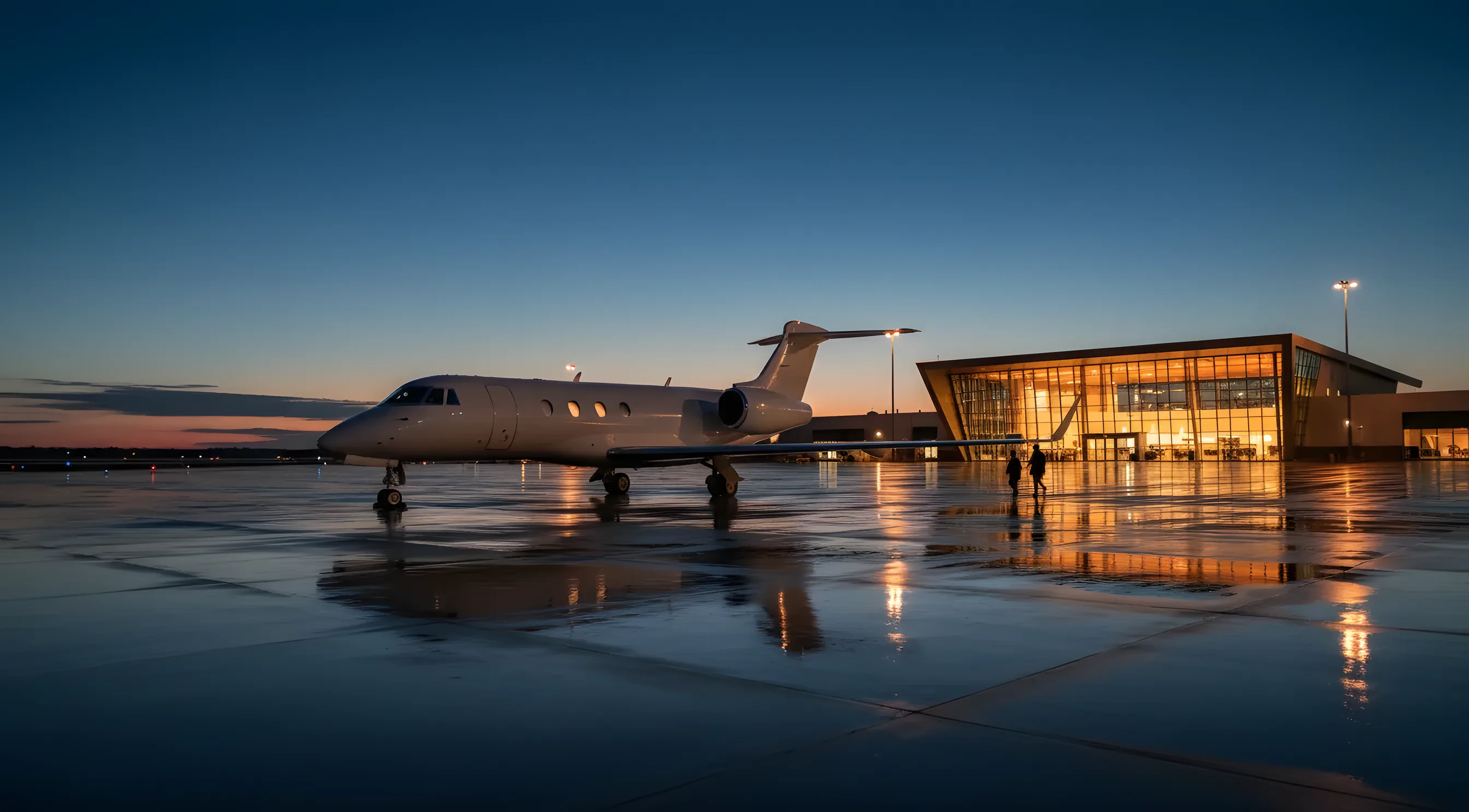 A private jet on an airport tarmac at dusk, with a modern terminal building in the background.