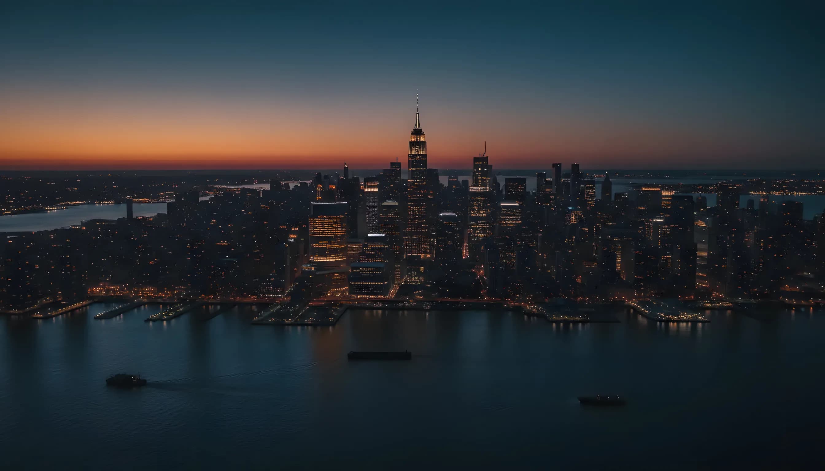 Aerial view of the Manhattan skyline at dusk with city lights reflecting on the water.