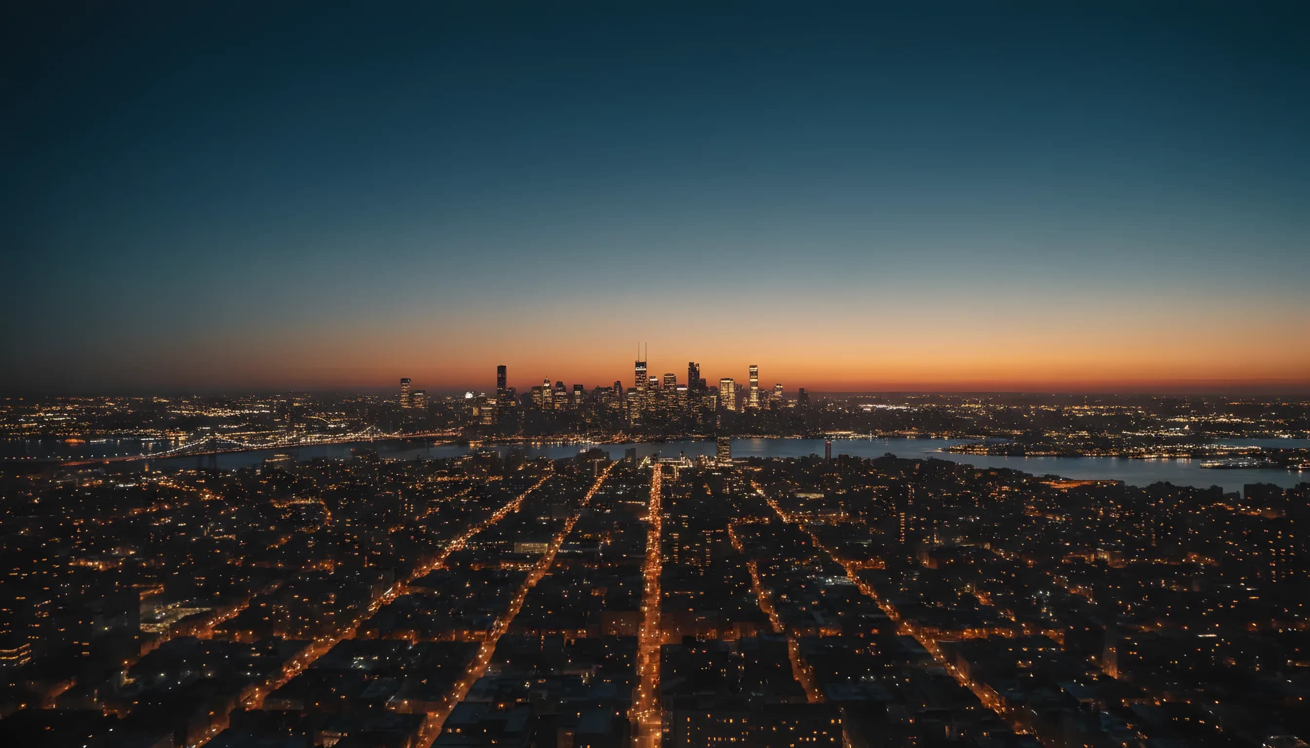 A helicopter flies over a city at dusk, with the Manhattan skyline visible in the distance.