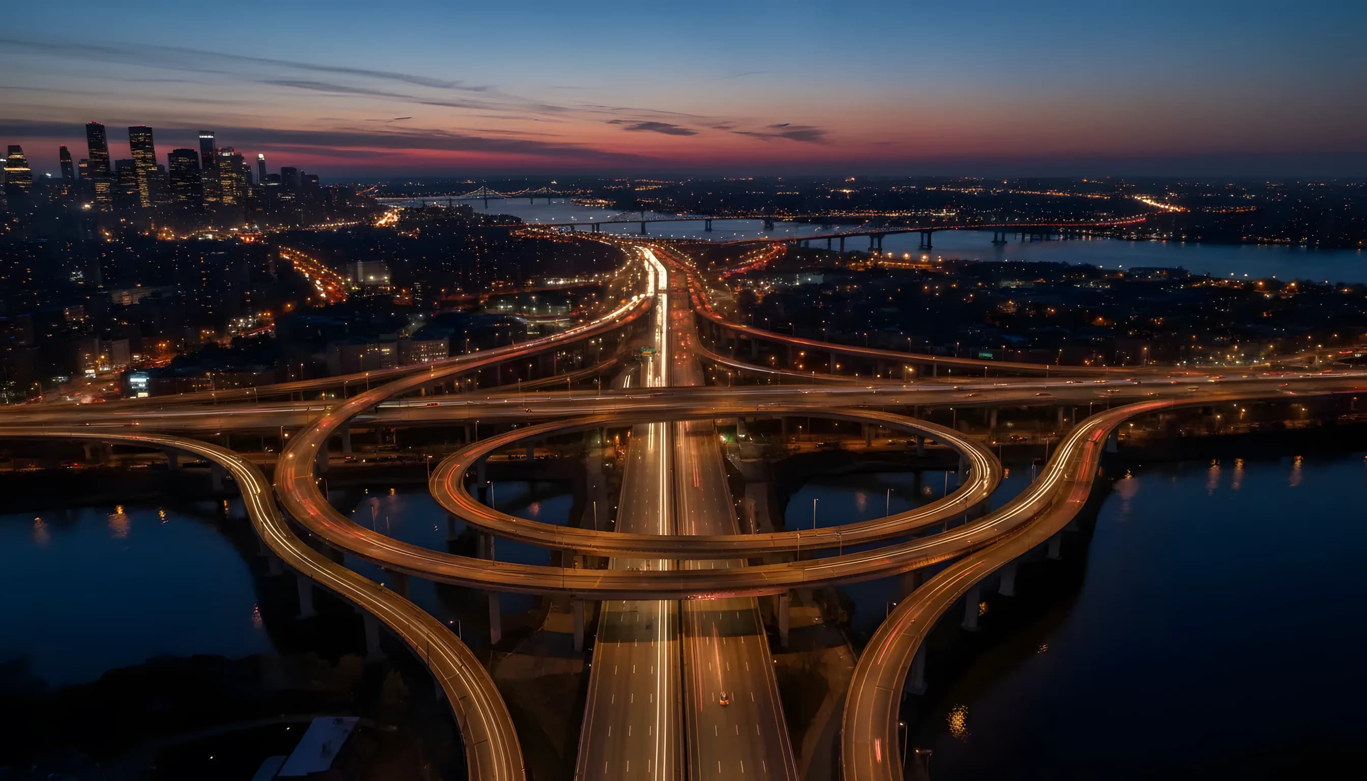 Aerial view of New York City bridges and highways illuminated at dusk, connecting Queens and the Bronx.