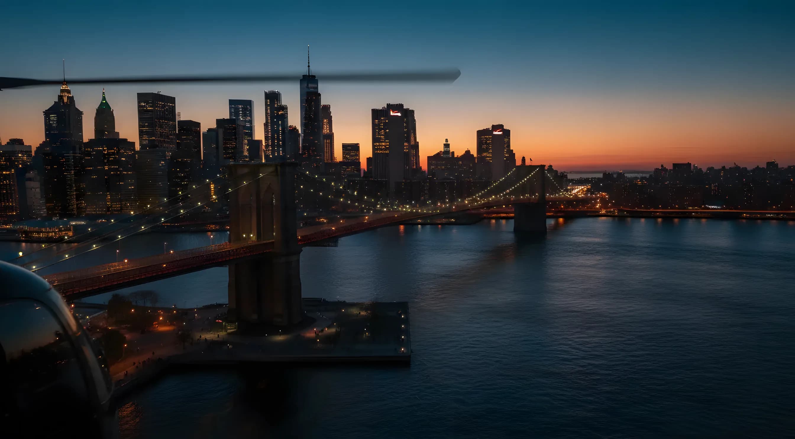 Aerial view of the Brooklyn Bridge and Manhattan skyline at dusk.