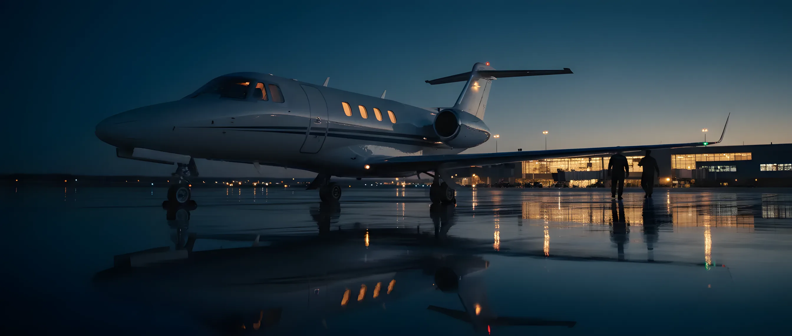 A private jet on an airport tarmac at dusk, with a glowing terminal in the background.