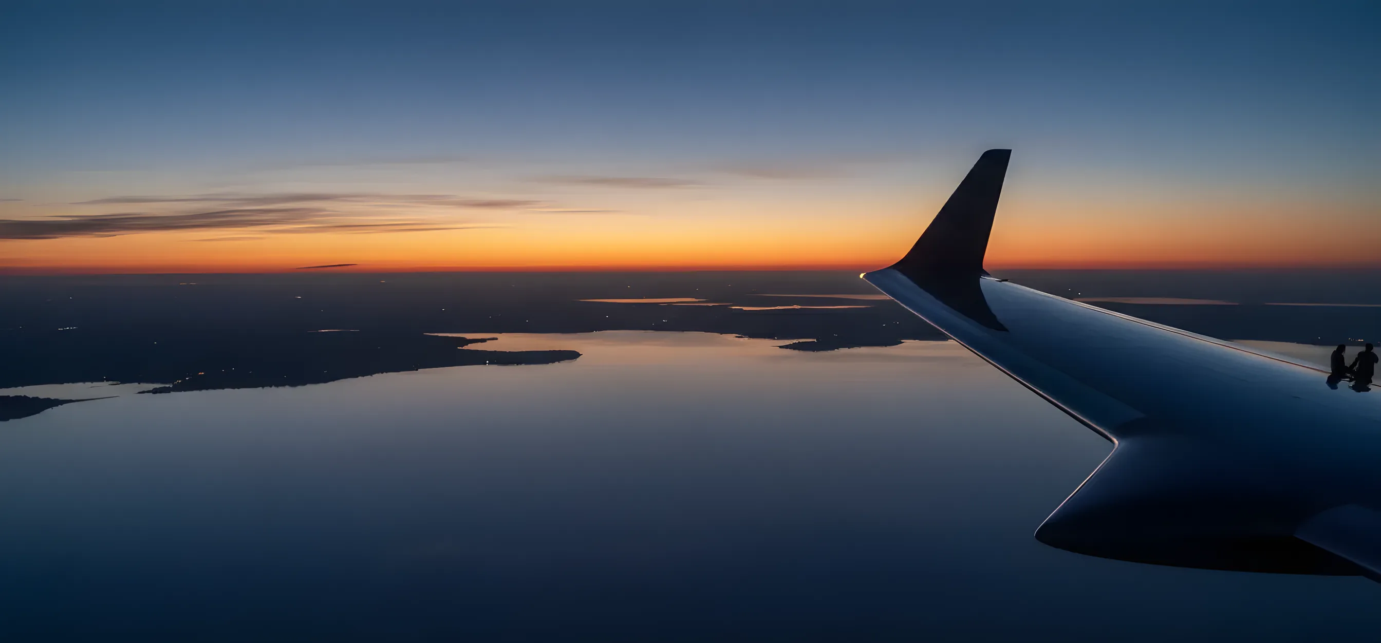 Aerial view from a private jet showing the wing over the calm blue water of a Great Lake.