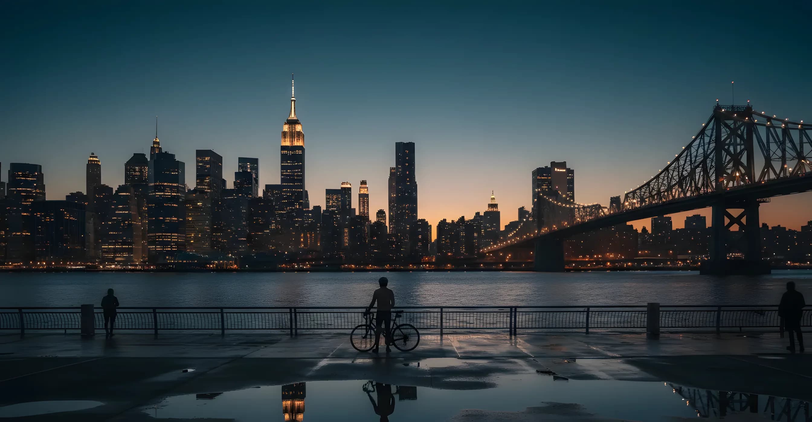 A cyclist on a Queens waterfront path at dusk facing the Queensboro Bridge and Midtown Manhattan.