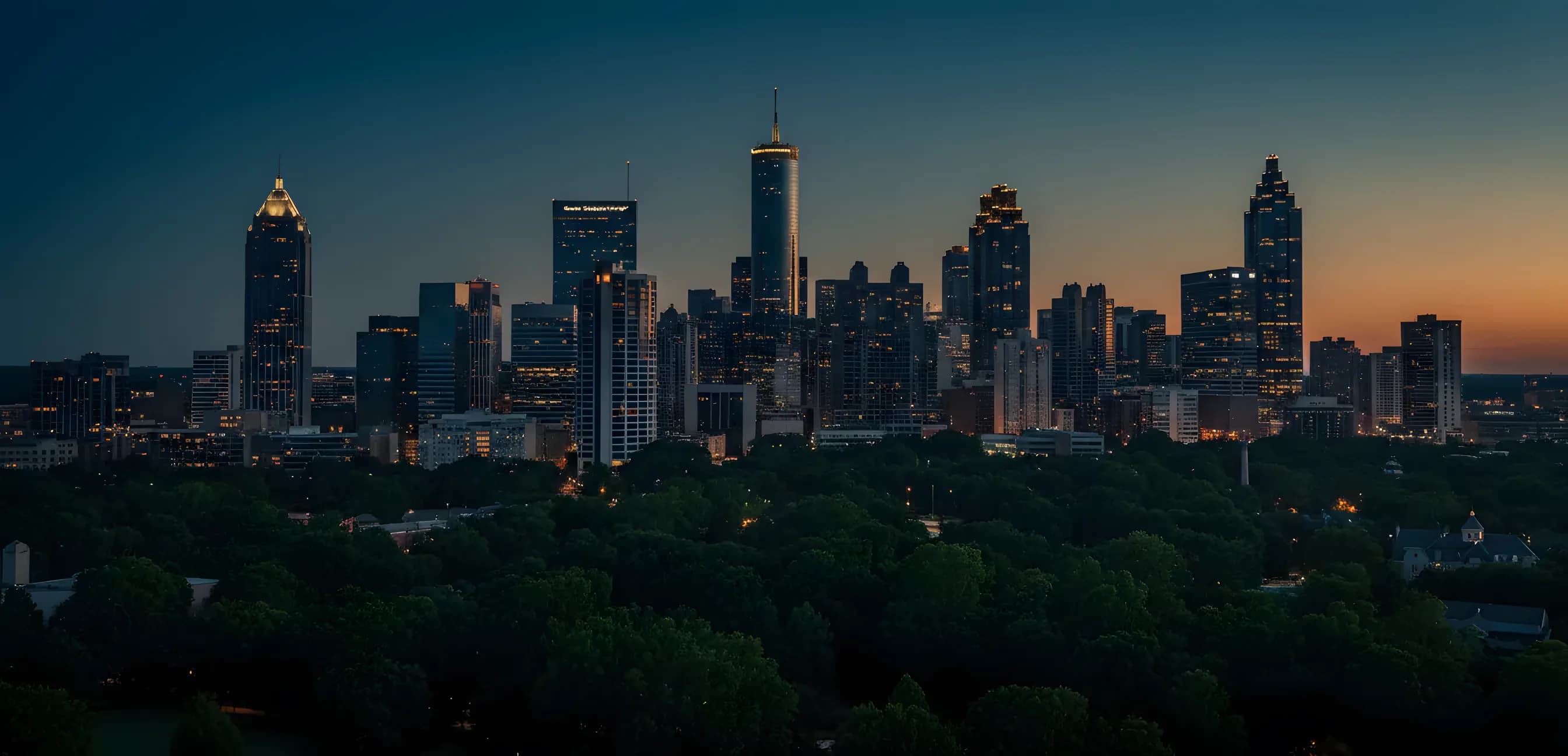 Aerial view of the Atlanta skyline rising above a green tree canopy at blue hour.
