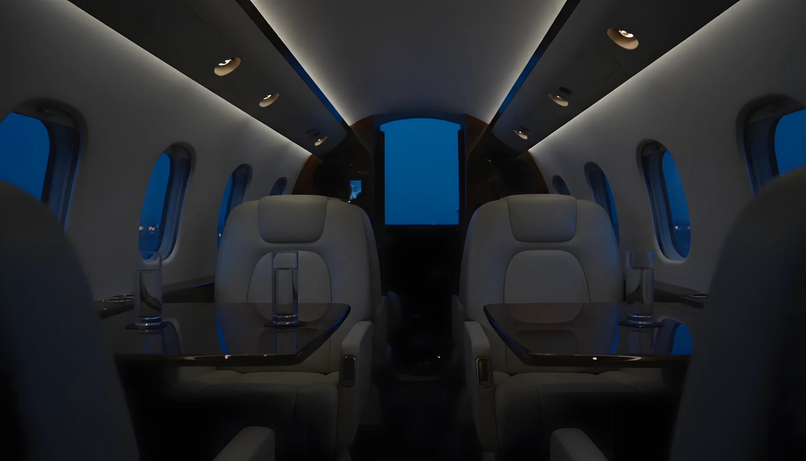 Cream leather club seats around a wood table in a business jet cabin at blue hour.