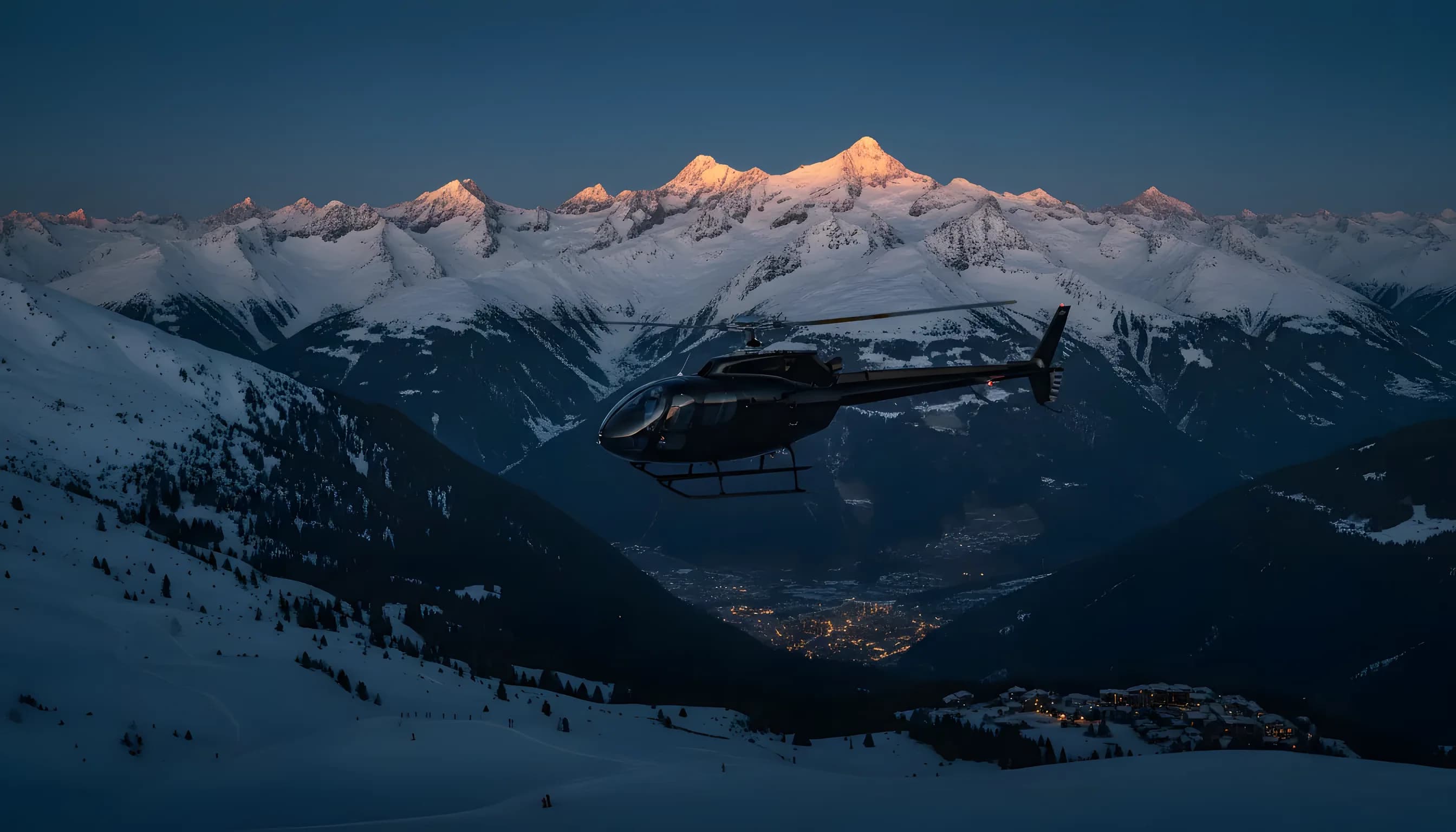 Hélicoptère survolant les Alpes enneigées au crépuscule, avec un village de ski illuminé au loin.