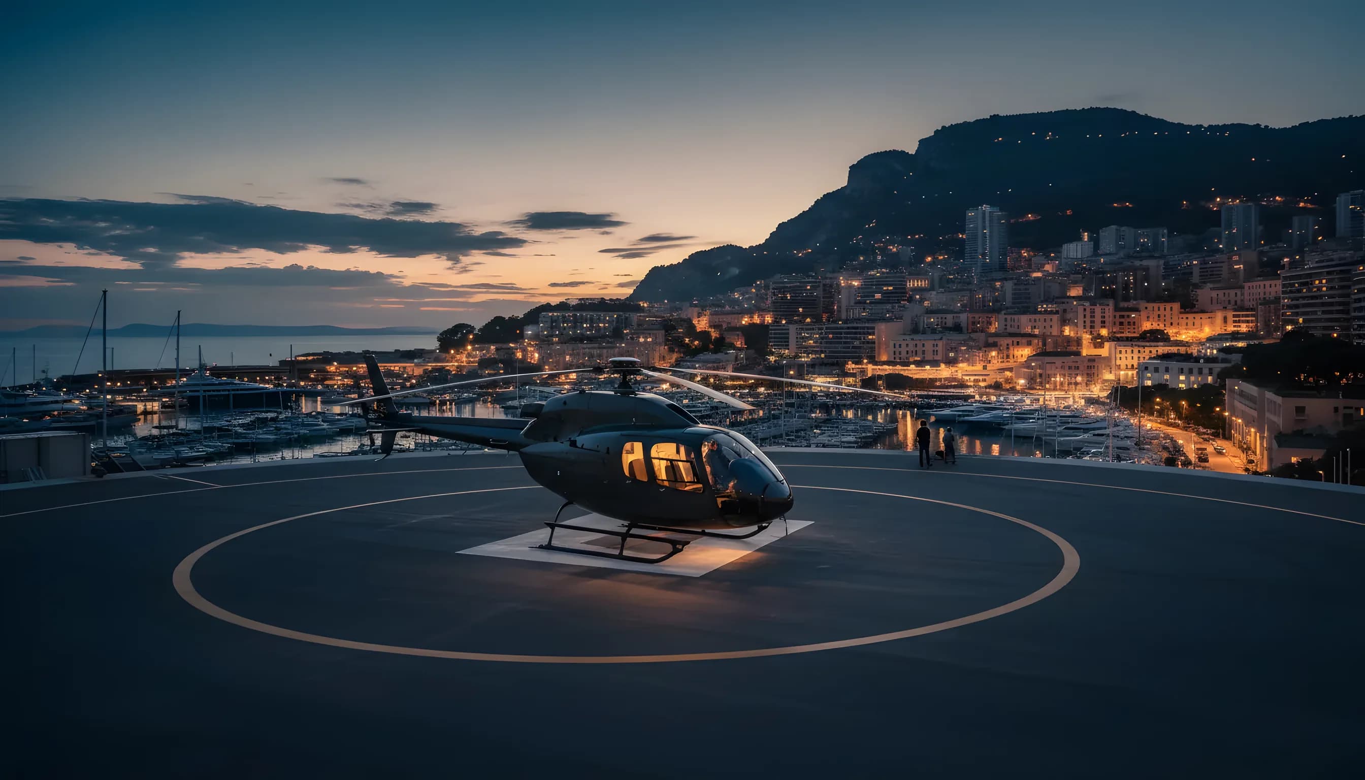 Héliport de Monaco au crépuscule, avec un hélicoptère sur la piste et les lumières de la ville en arrière-plan.