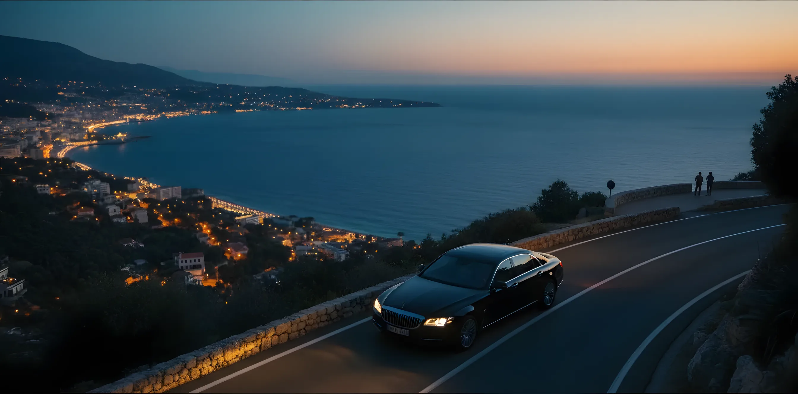 Une berline de luxe sur une route côtière la nuit, avec vue sur le littoral illuminé de la Côte d'Azur.