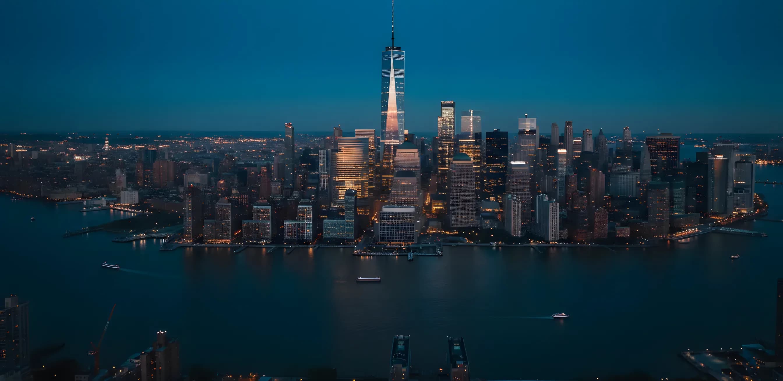 Aerial view of the Lower Manhattan skyline and One World Trade Center at blue hour.