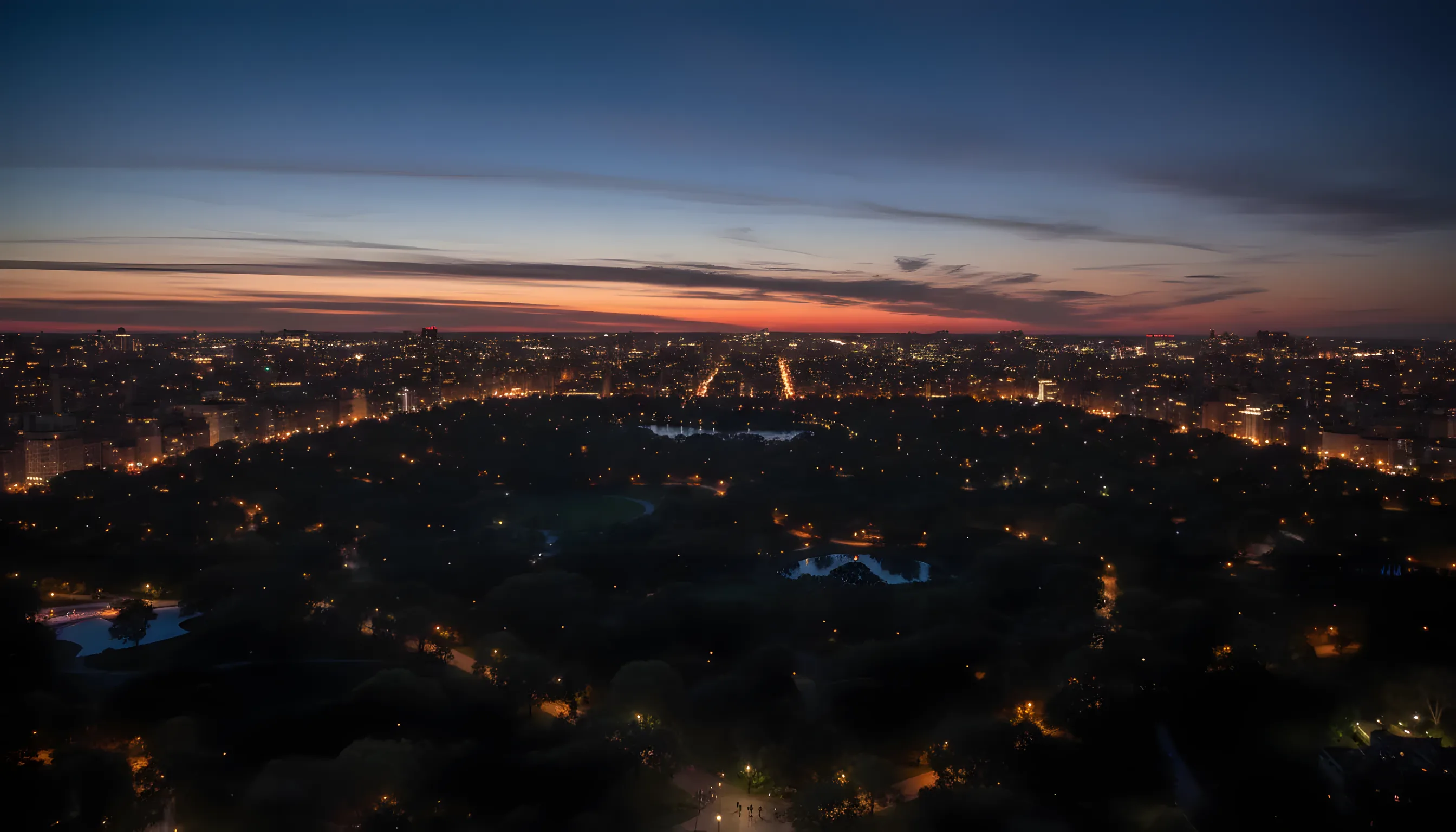 An aerial view of Harlem, New York City, at dusk, with city lights illuminating the streets and buildings.
