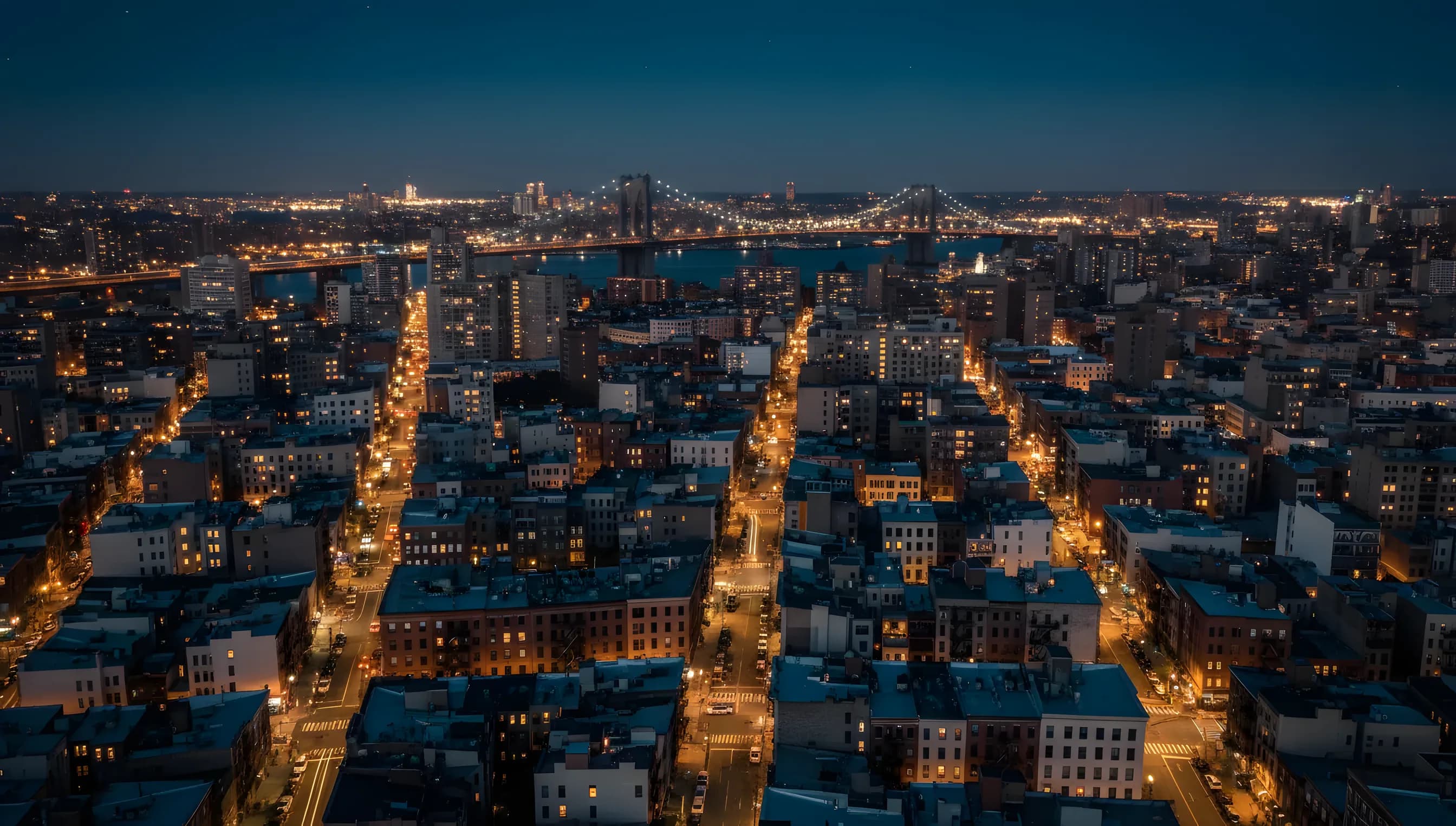 Aerial view of the Lower East Side in New York City at dusk, with city lights glowing against a dark blue sky.