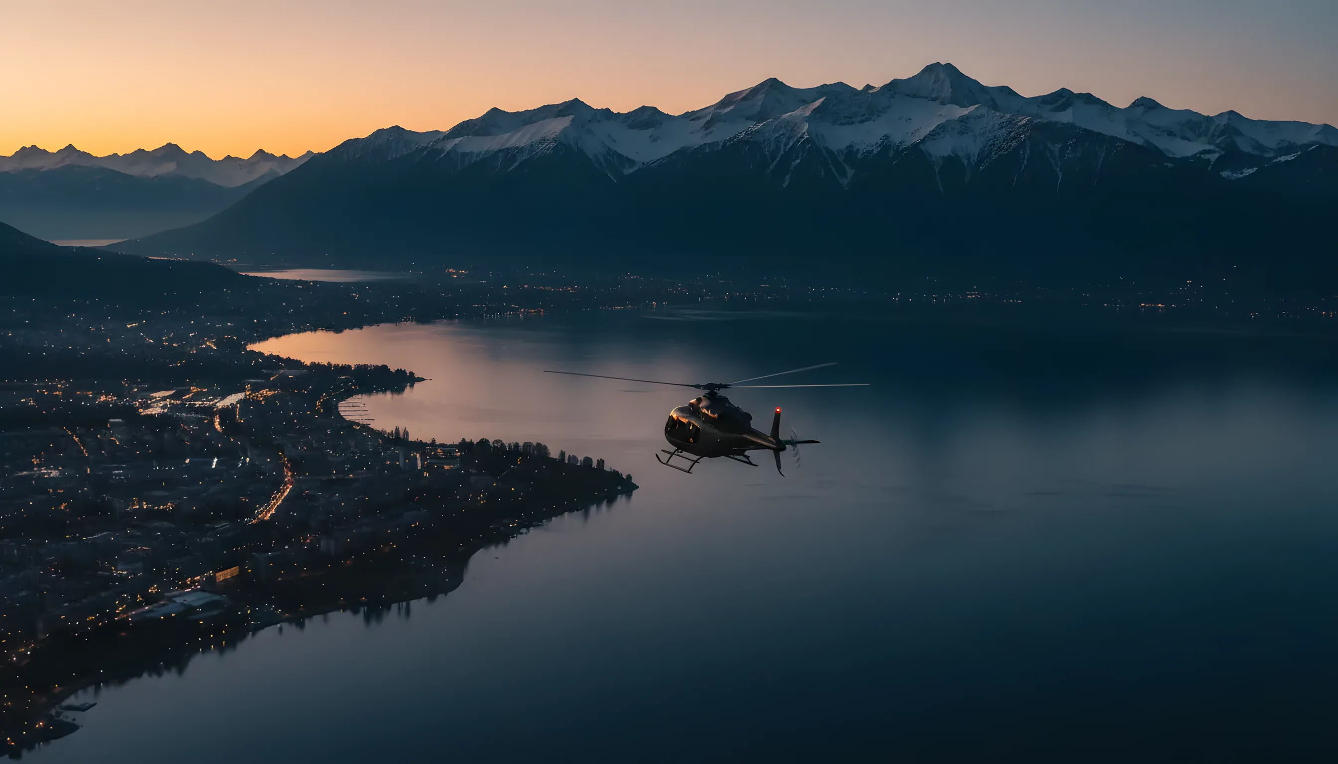 A helicopter flies over Geneva at twilight, heading towards the snow-capped Alps.
