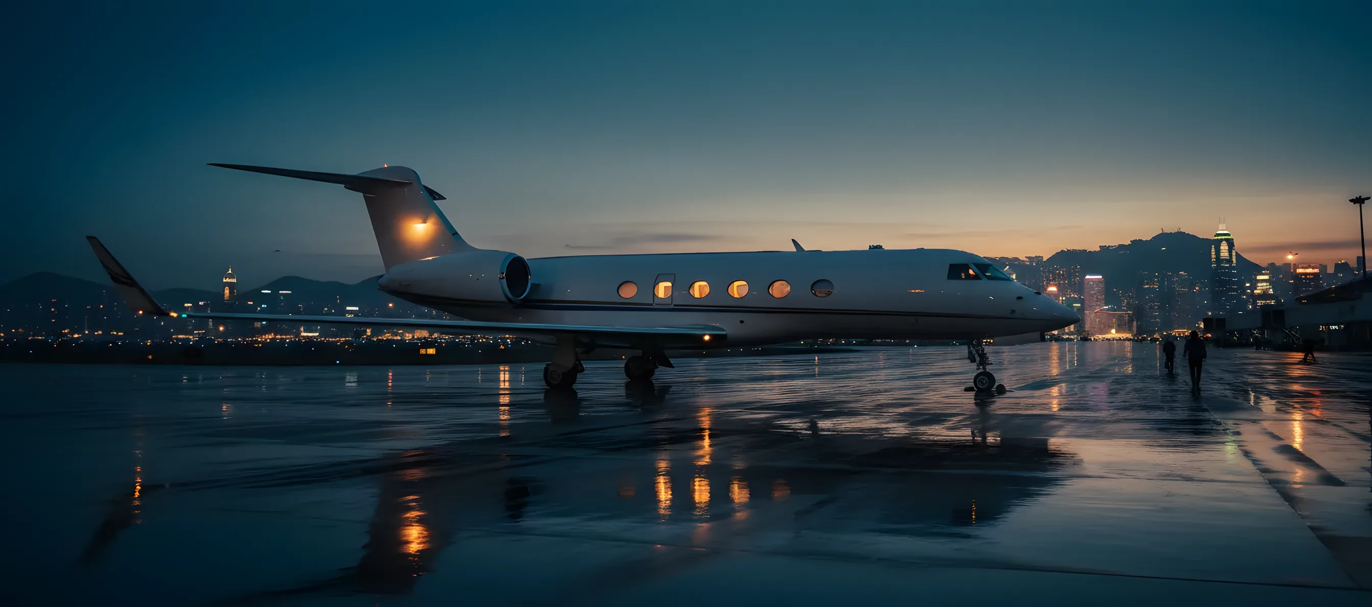 A private jet on a tarmac at dusk with the lights of a distant city skyline in the background.