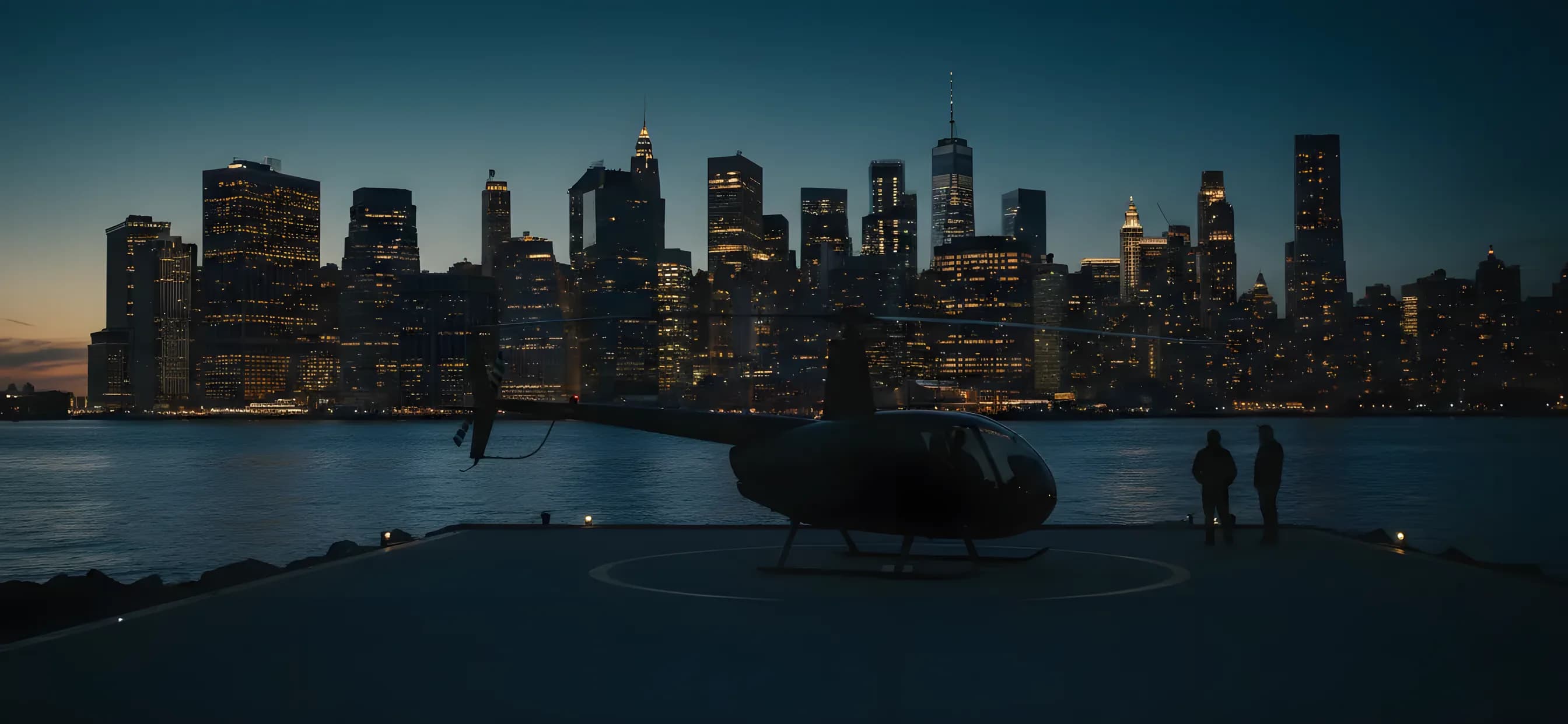 A helicopter on a helipad at dusk with the Lower Manhattan skyline in the background.