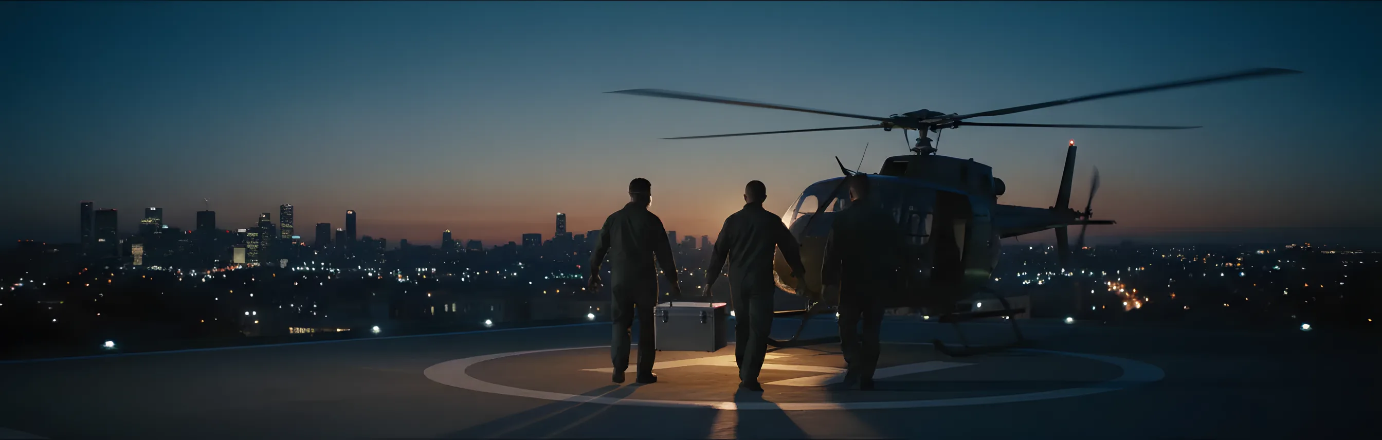 Medical personnel carry an organ transport container to a helicopter on a city rooftop at dusk.