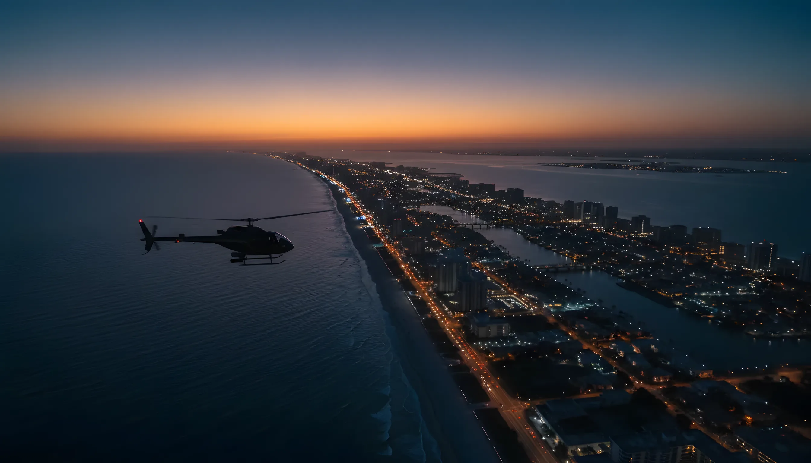 Aerial view of a helicopter flying north along the Florida coast at twilight, with city lights visible.