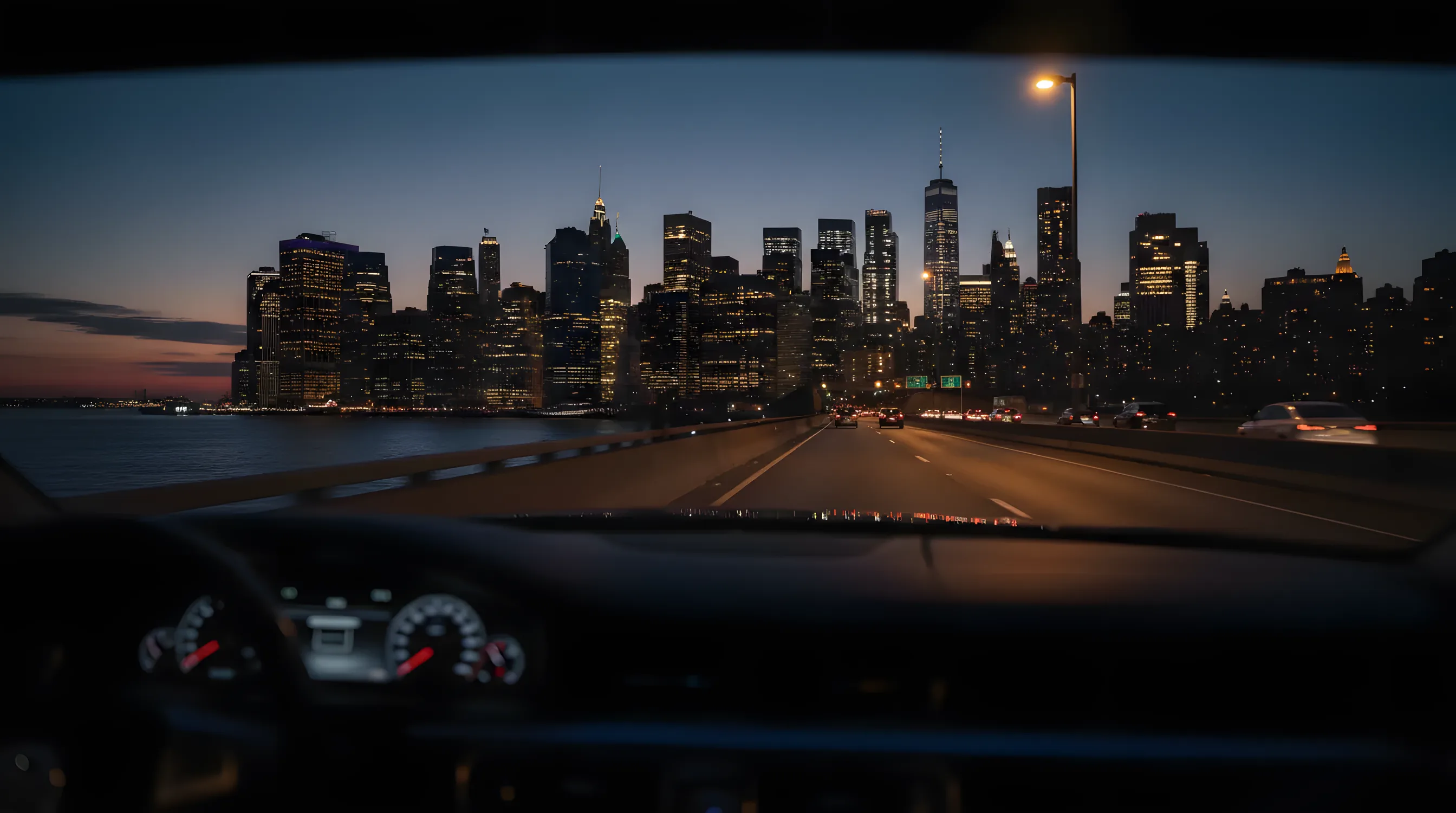 The Manhattan skyline viewed from a car on a highway at dusk.