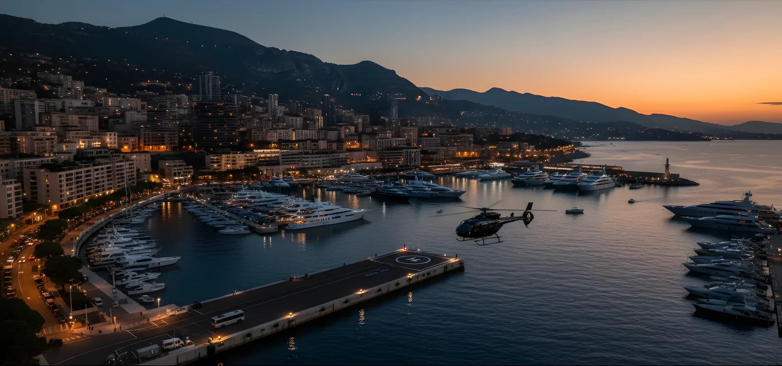Aerial view of superyachts in Monaco's Port Hercule at dusk, with a helicopter flying overhead.