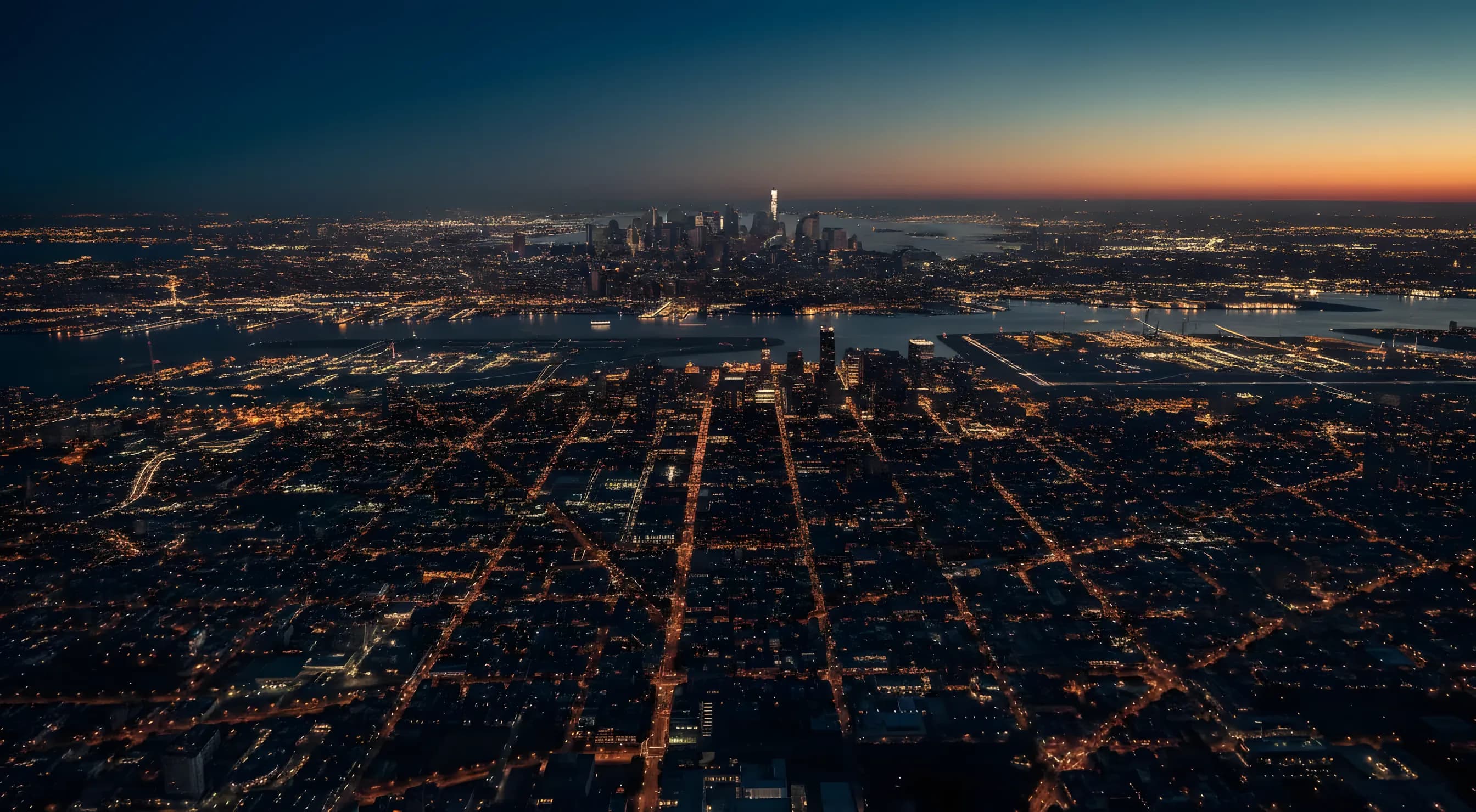 Sweeping aerial view of the New York City area at dusk, with the lights of two airports visible in the distance.