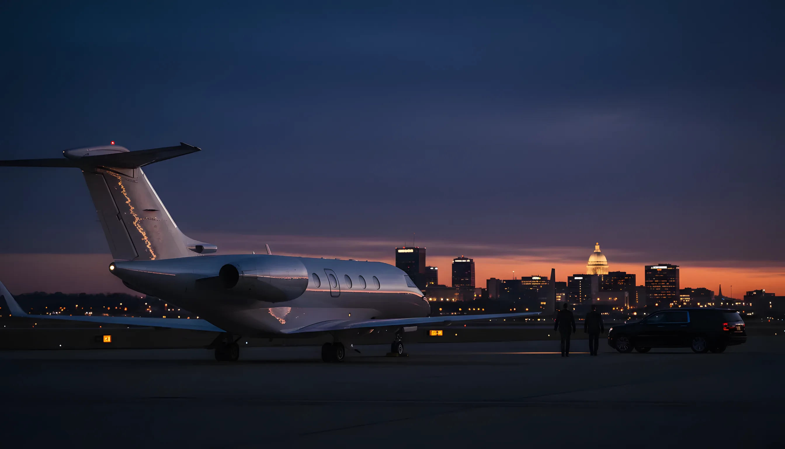 A private jet on an airport tarmac at dusk, with the Jackson, Mississippi skyline in the background.