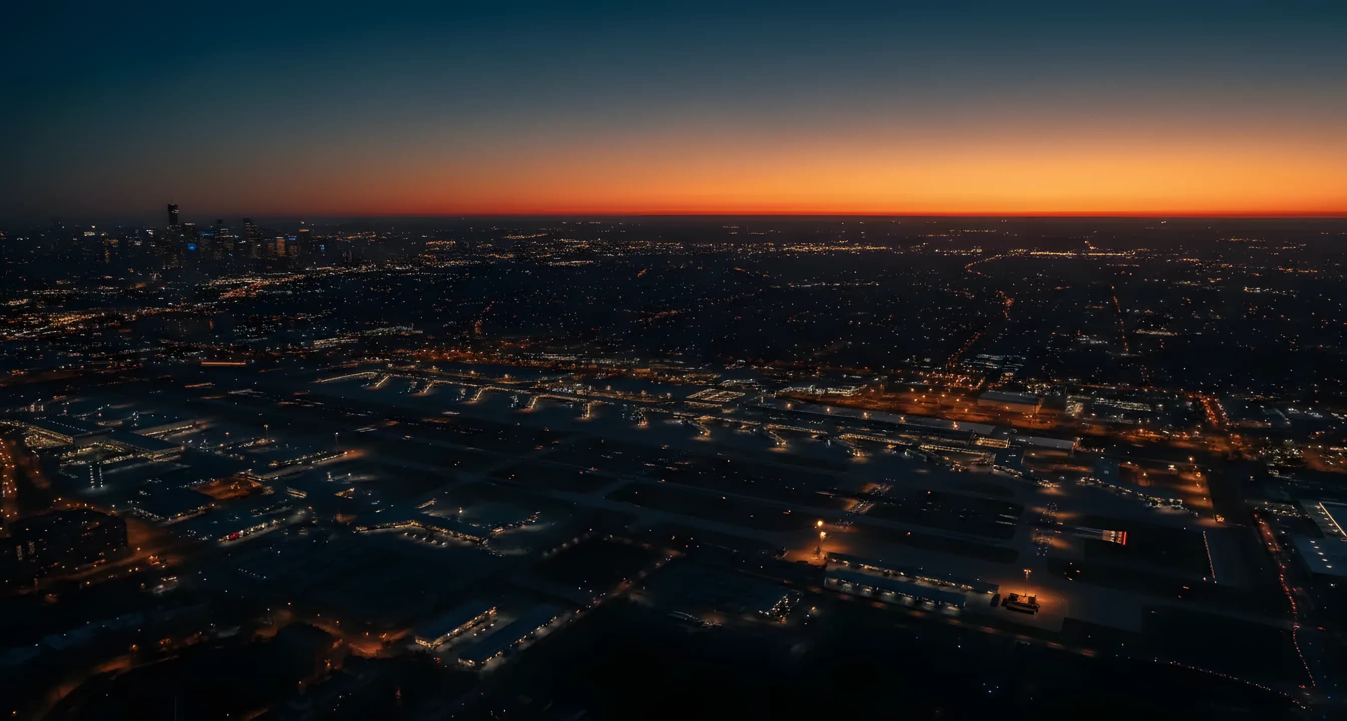 Aerial view of New York City and Long Island at dusk, with city lights glowing under a dark blue sky.