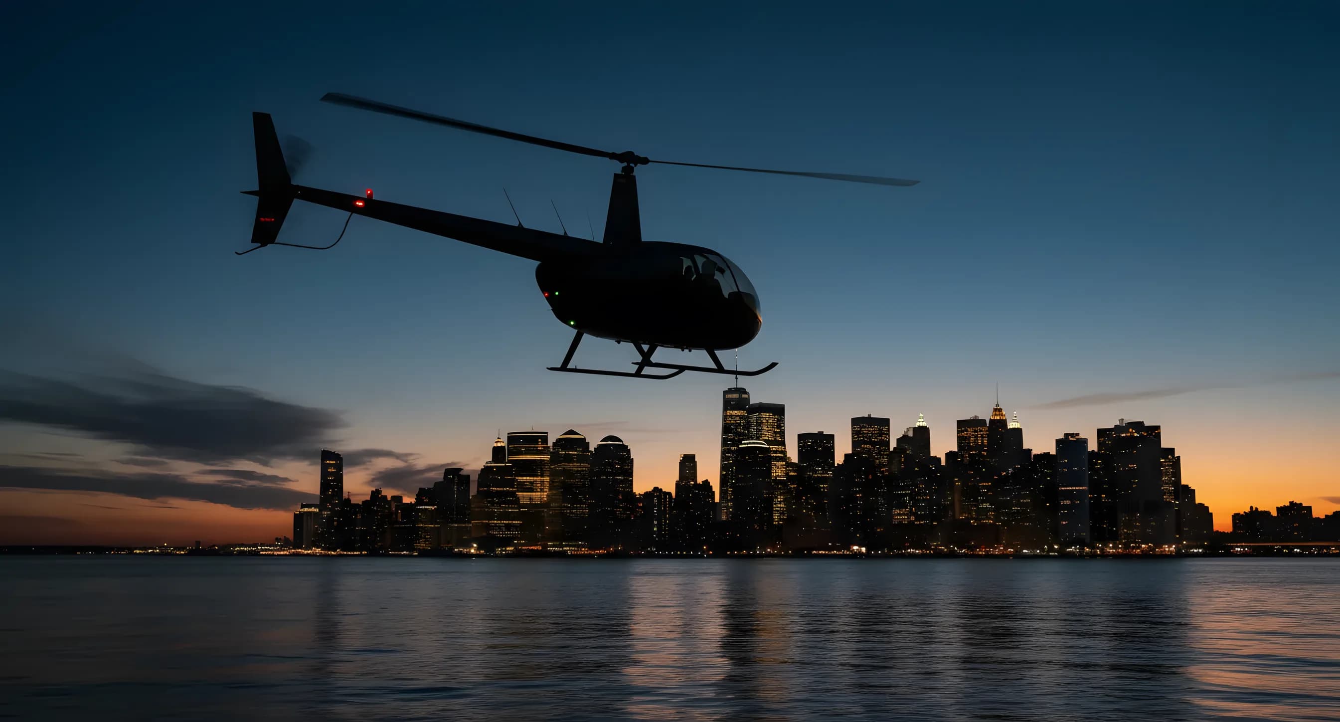 A helicopter flies over water at dusk, with a distant city skyline glowing in the background.