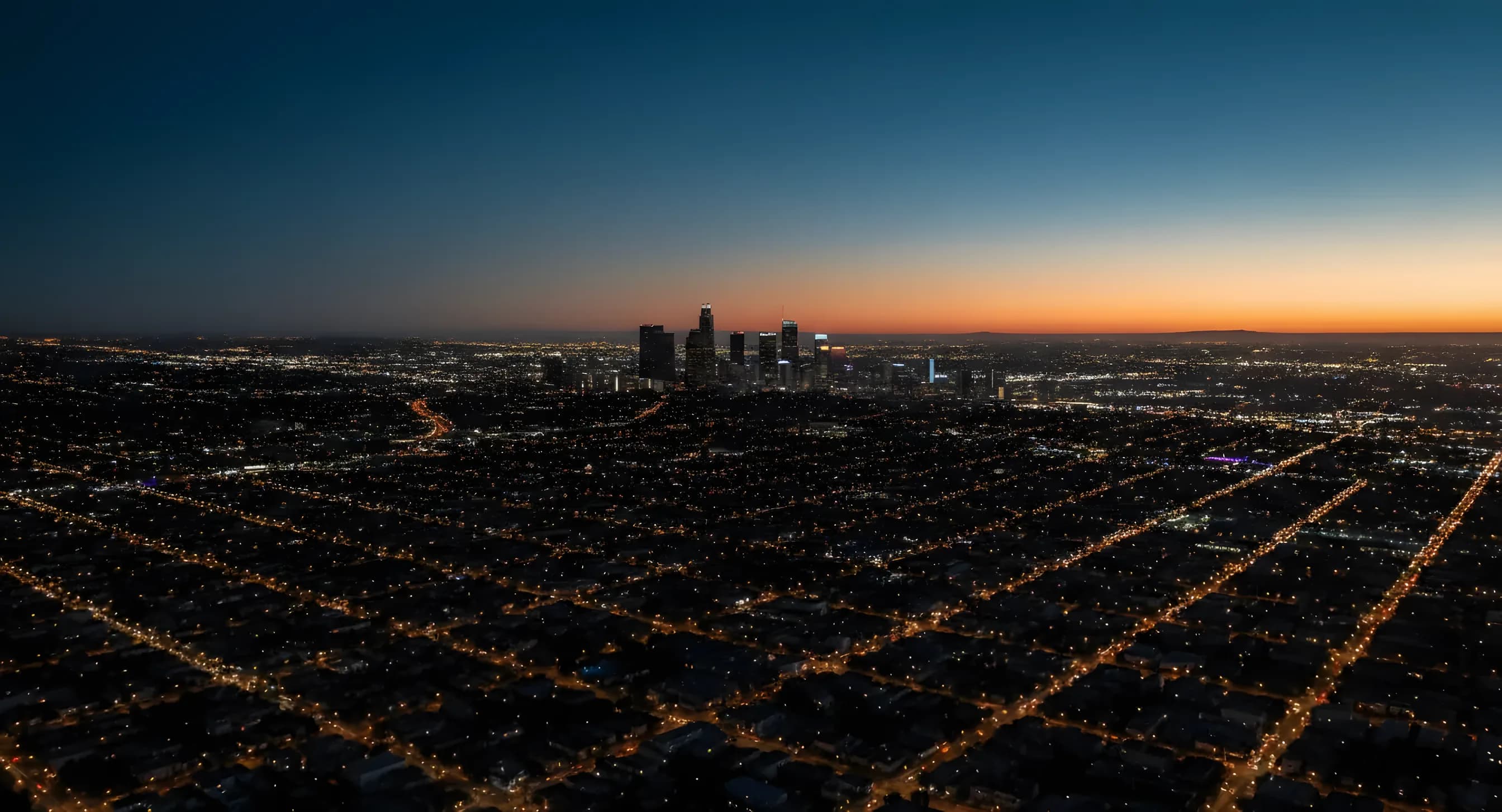 Aerial view of the Los Angeles city grid and downtown skyline at twilight.