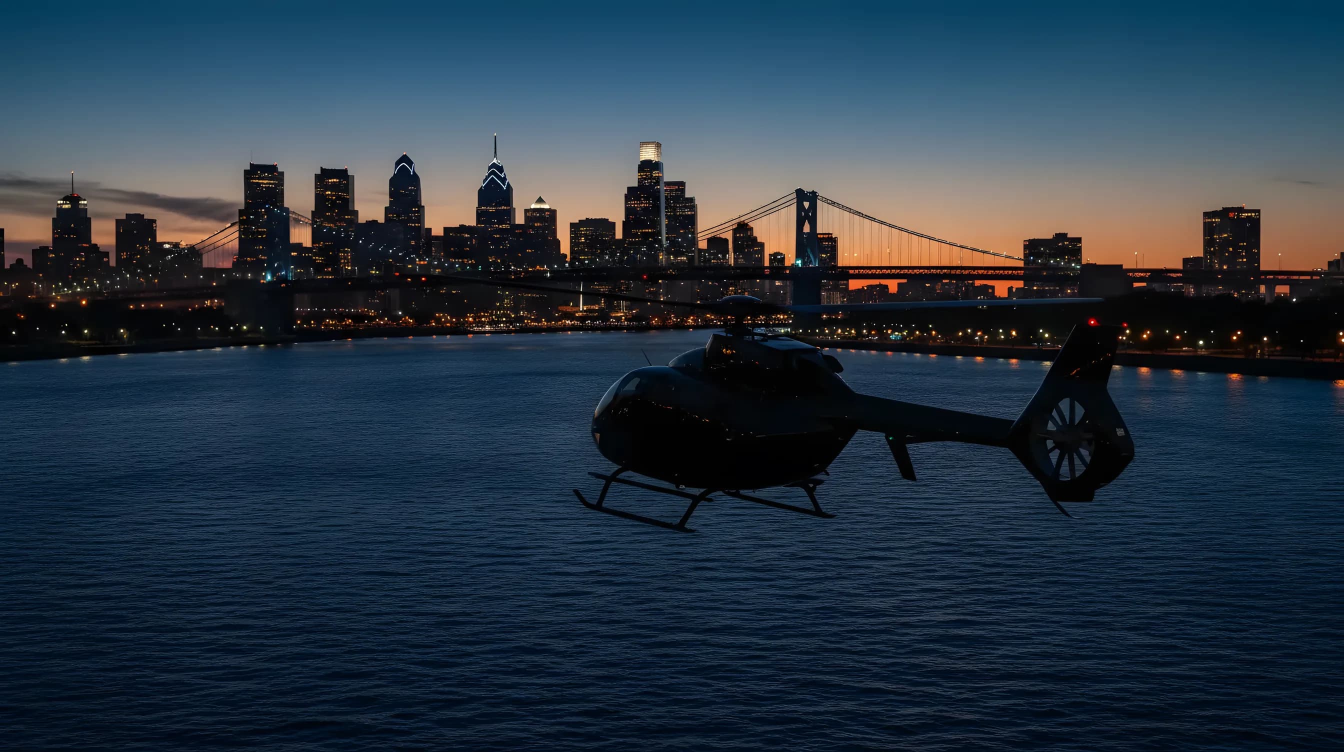 A helicopter flies toward the Philadelphia skyline over a river at dusk.