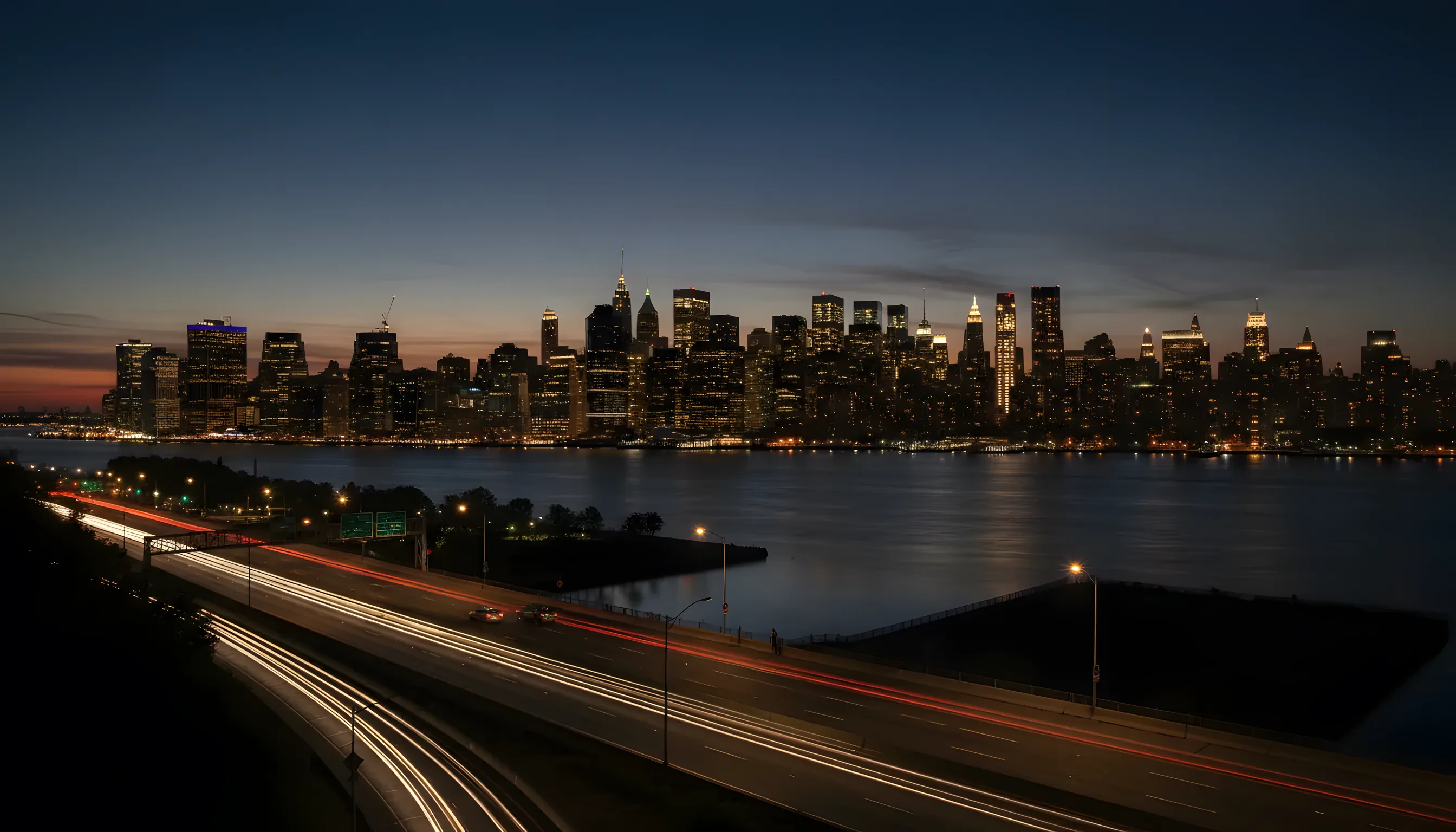 The Manhattan skyline glows with amber lights against a deep blue evening sky, viewed from across the water in New Jersey.