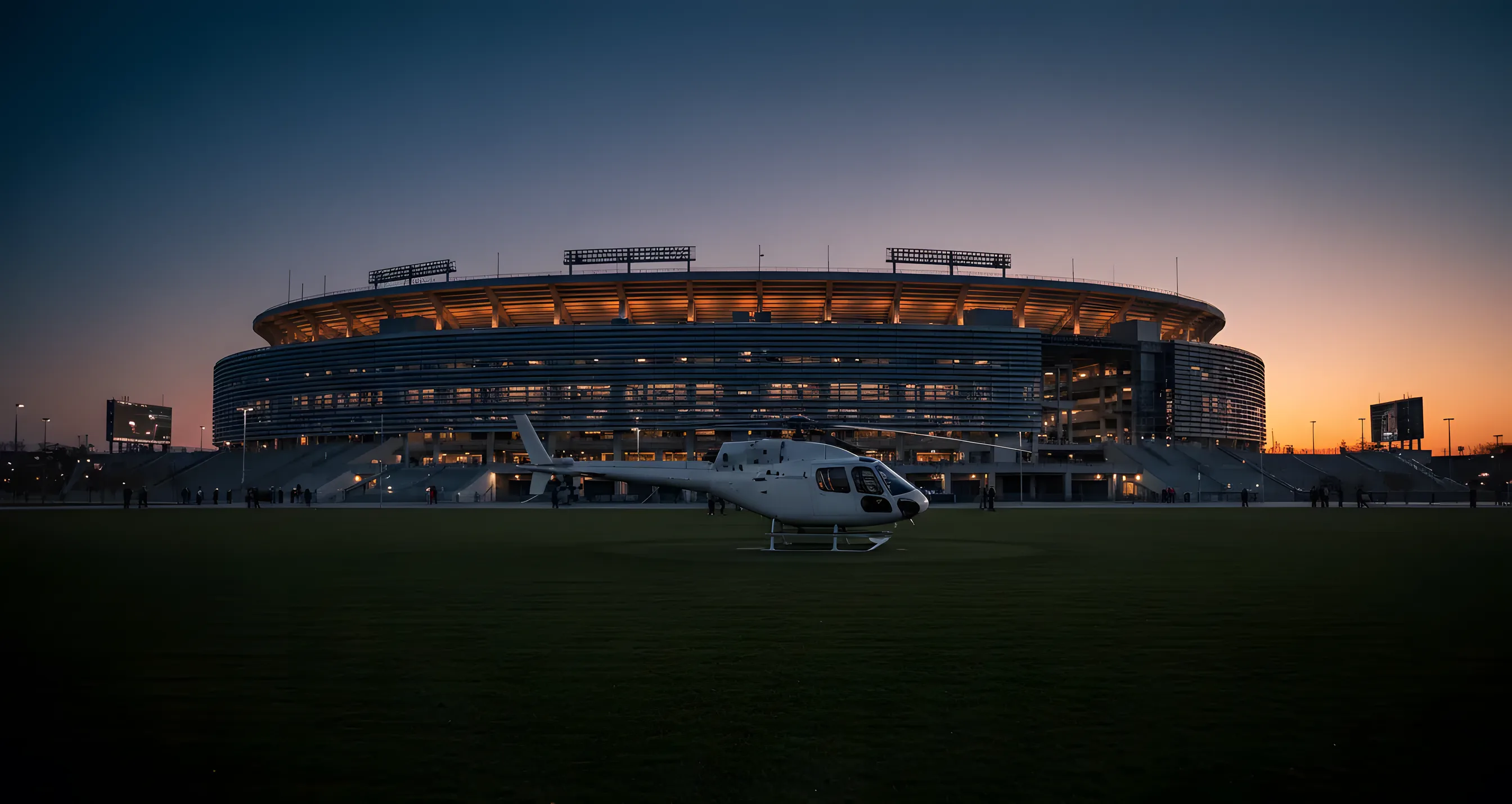 A plain white helicopter on a grassy pad with MetLife Stadium behind it on a sunny day.