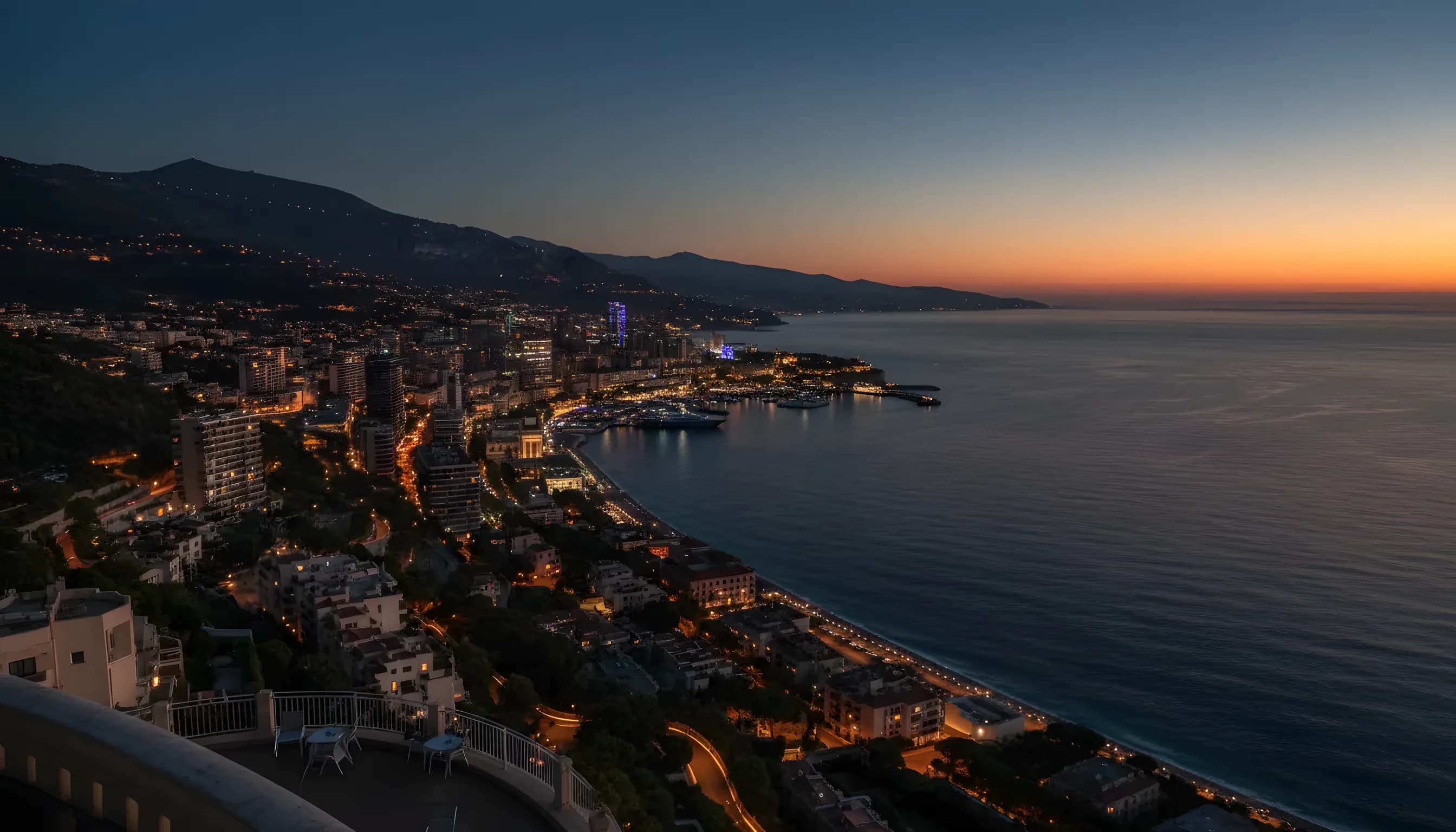 Aerial view of the Monaco coastline and harbor at twilight, with city lights beginning to glow.