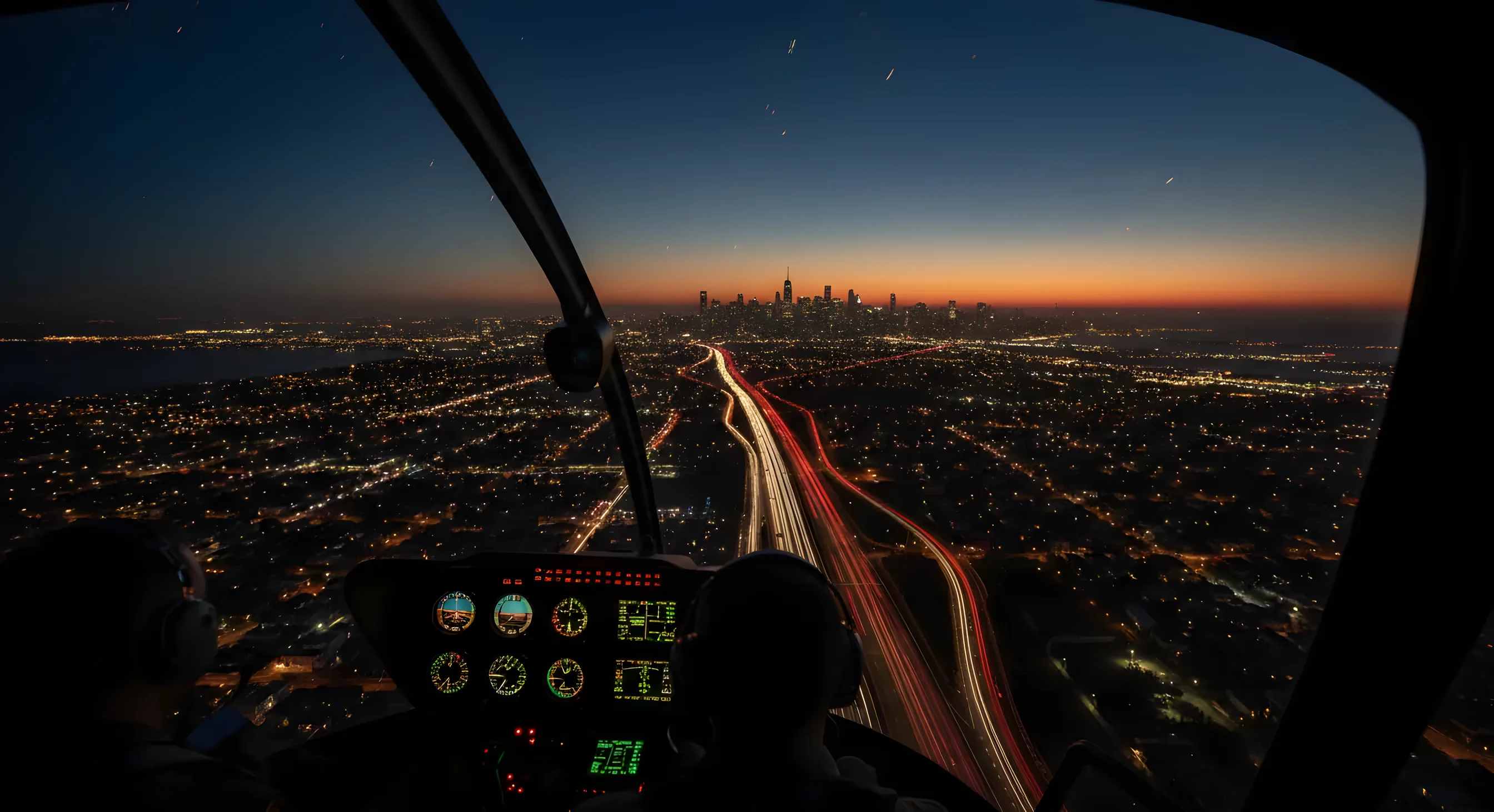 Aerial view of a highway at dusk with light trails from traffic, with a city skyline glowing in the distance.