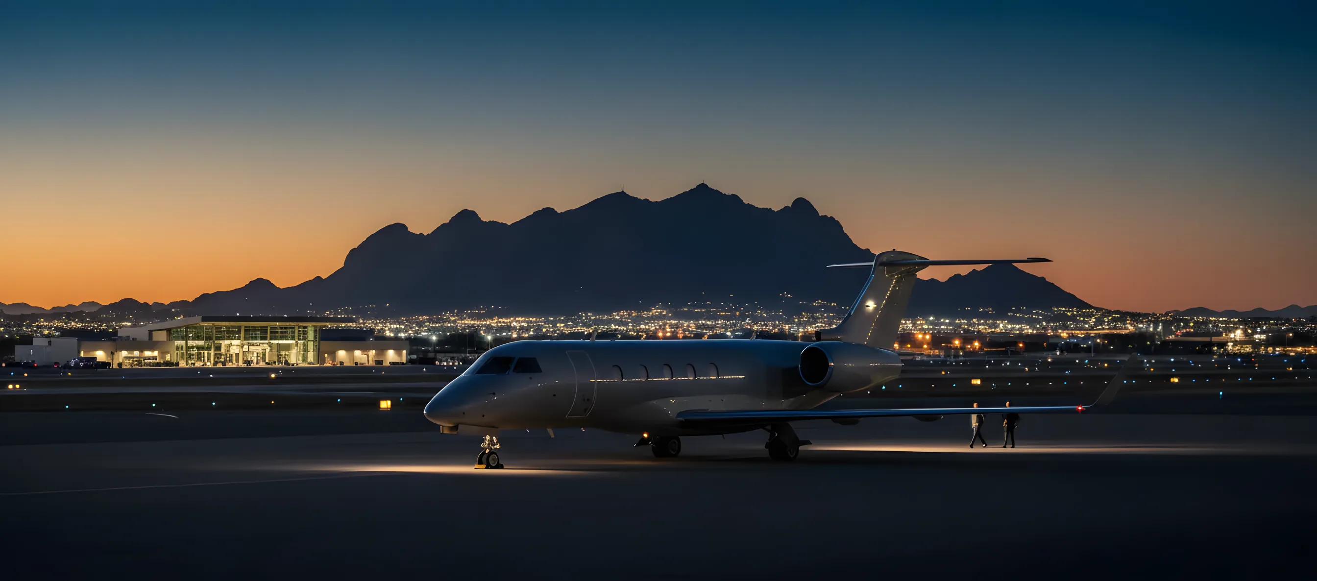 A private jet on an airport tarmac at dusk, with the Phoenix mountains and city lights in the background.