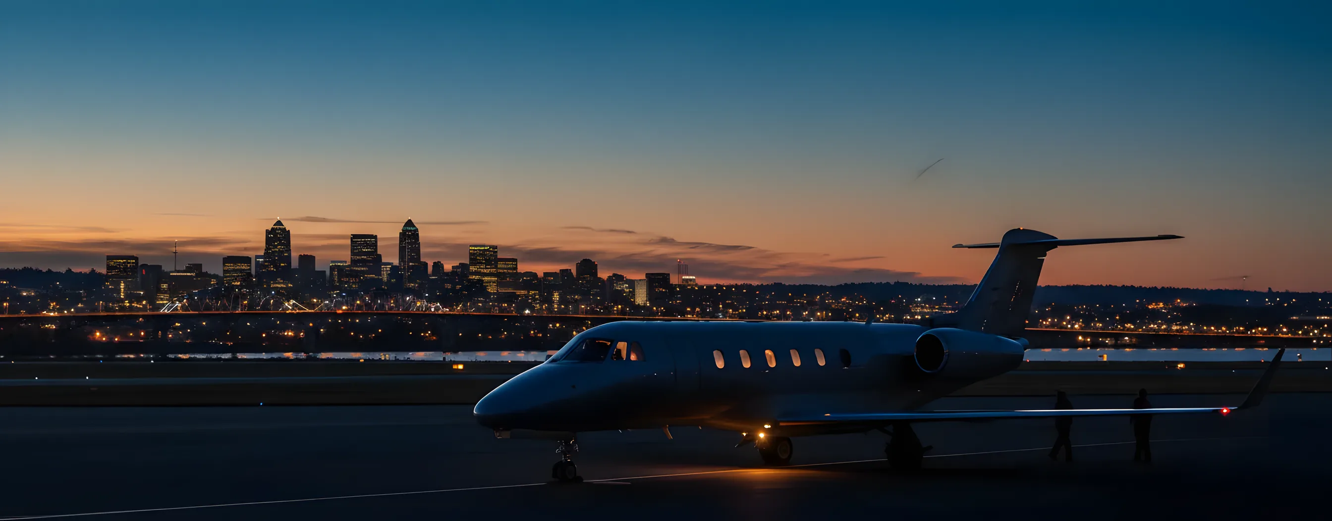A private jet on an airfield at dusk, with the Portland city skyline glowing in the background.