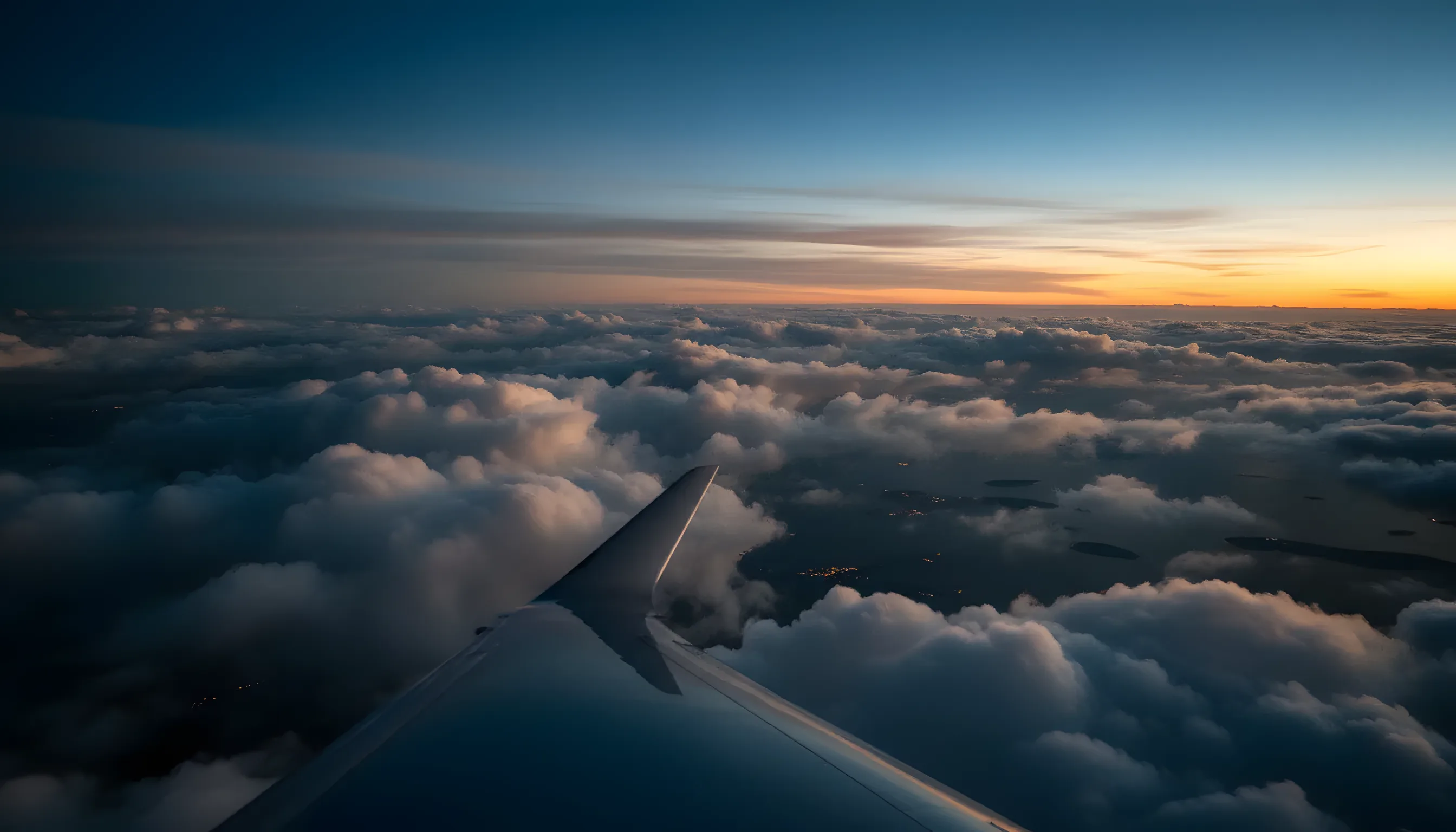 View from a private jet window, showing the wing over a sea of white clouds and blue sky.
