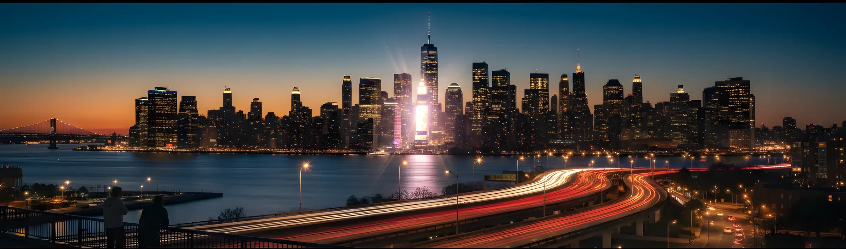 The Midtown Manhattan skyline at dusk, viewed from New Jersey with highway light trails in the foreground.
