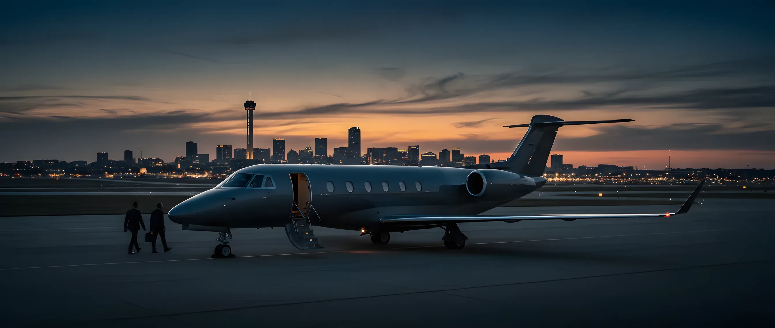 A private jet on an airfield at dusk, with the San Antonio skyline glowing in the background.