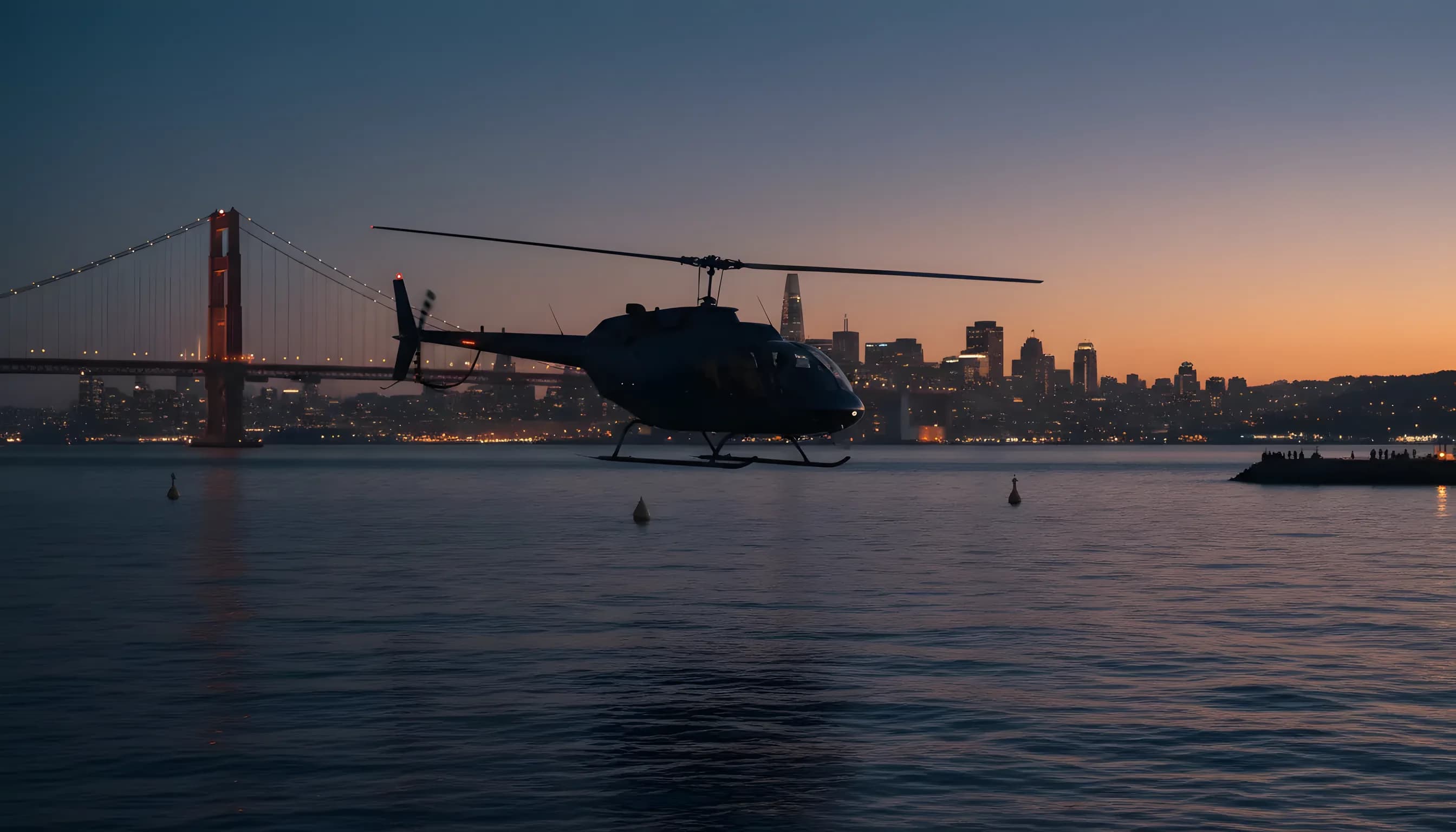 A helicopter flies over the San Francisco Bay at dusk, with the Golden Gate Bridge and city skyline in the background.