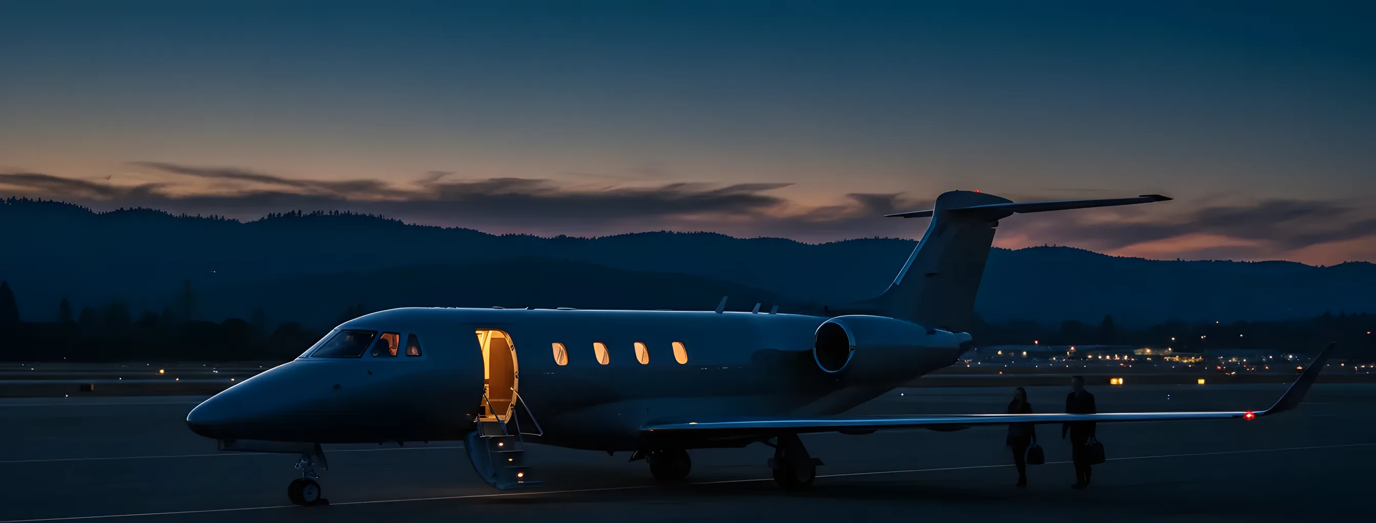 A private jet on an airport tarmac at dusk, with the silhouette of rolling hills in the background.