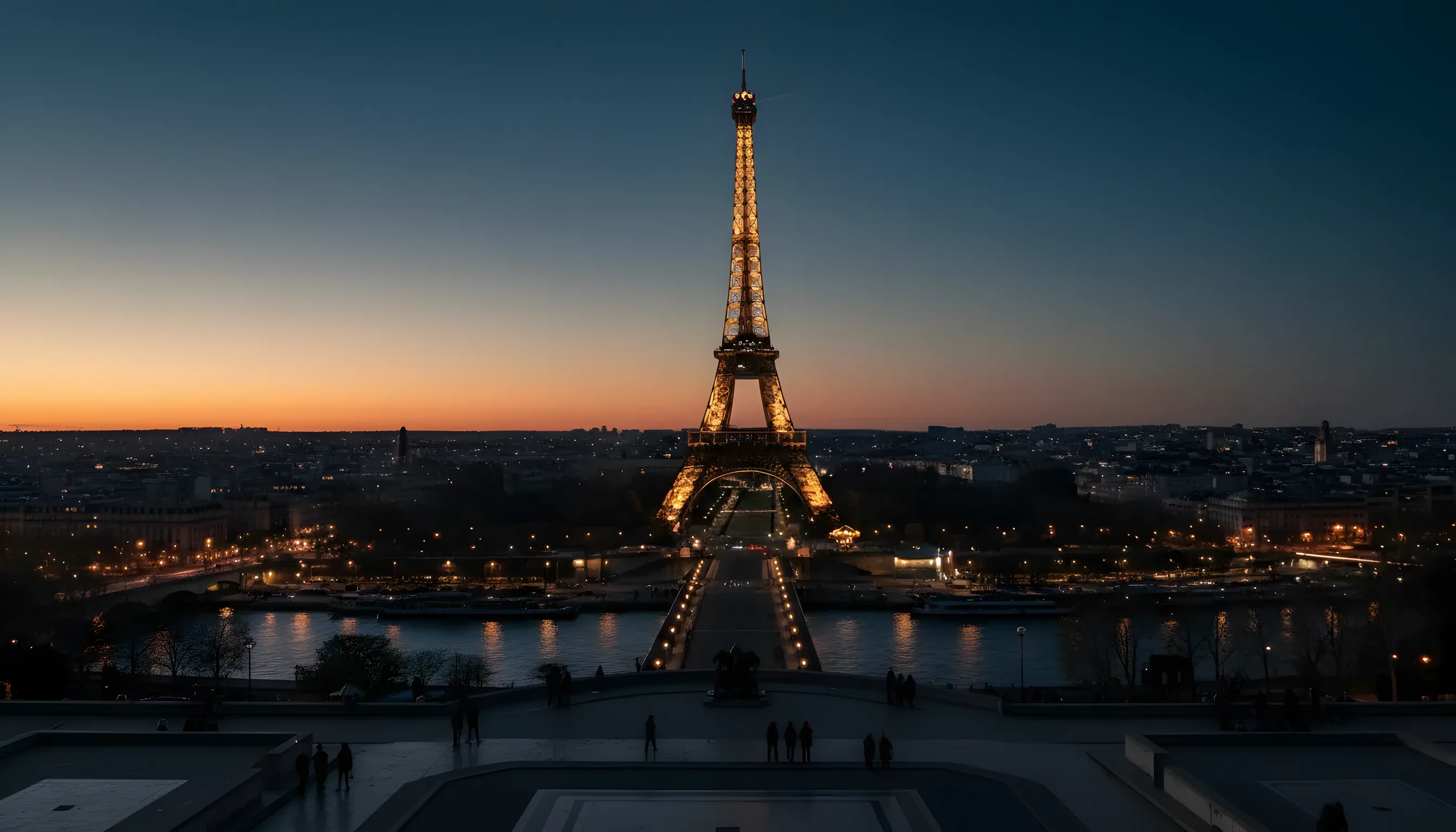 The Eiffel Tower lit golden above the Seine at blue hour.