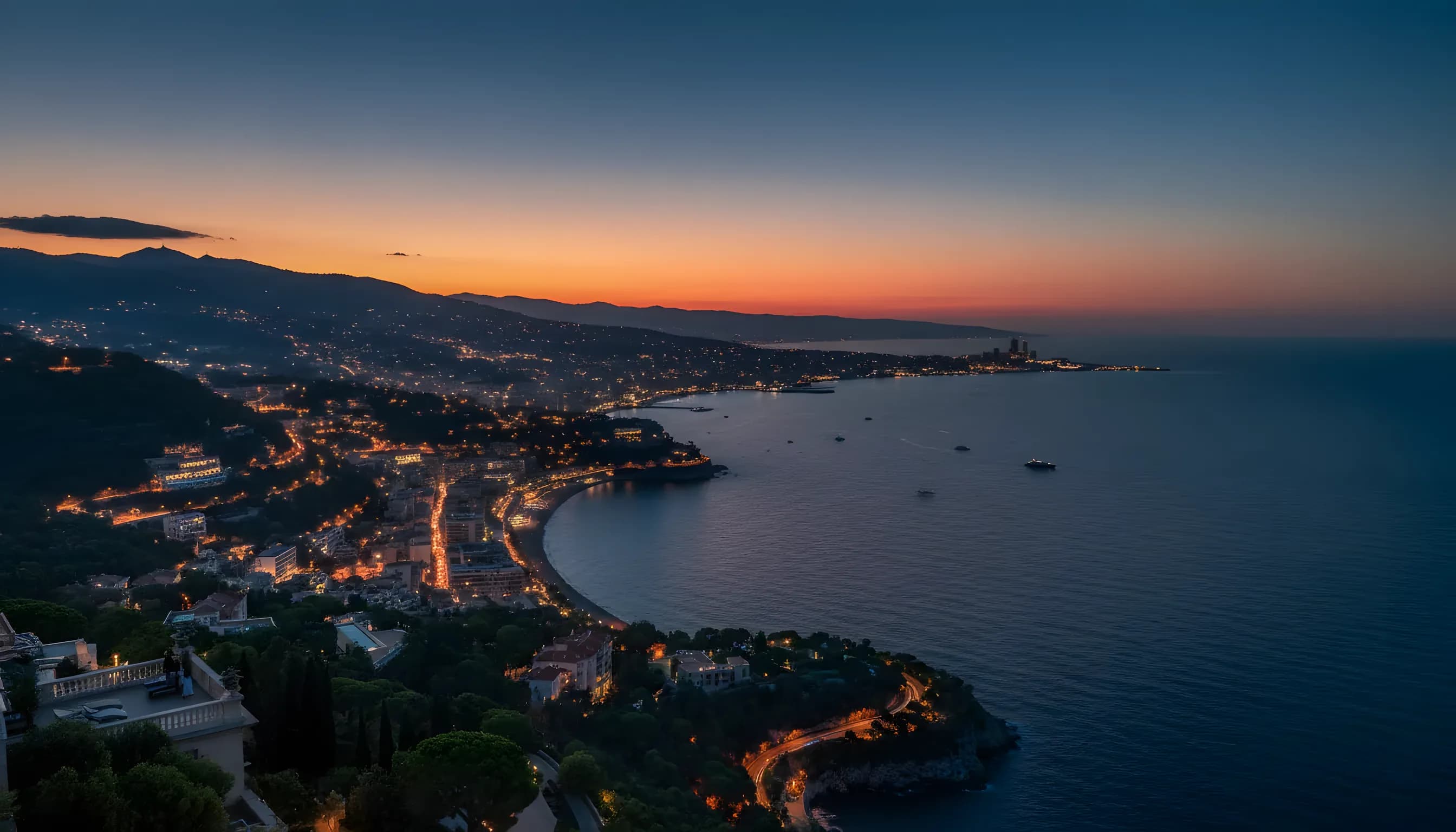 Aerial view of the French Riviera coastline at dusk, with city lights glowing between Nice and Monaco.