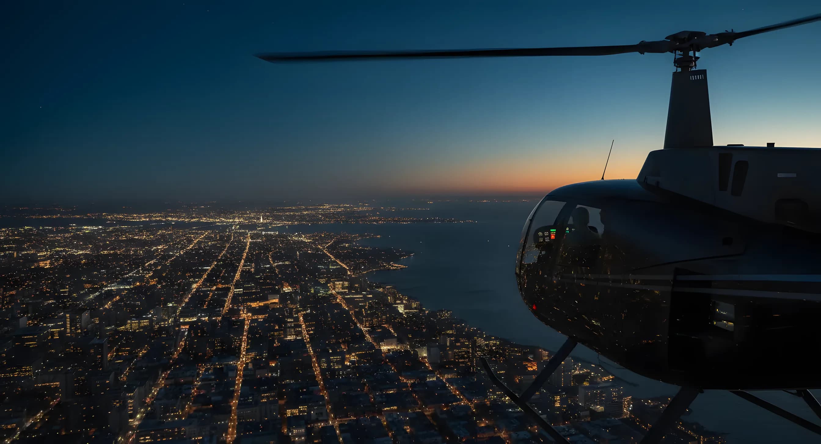 Aerial view from a helicopter flying over a coastline at dusk, with sprawling city lights visible below.