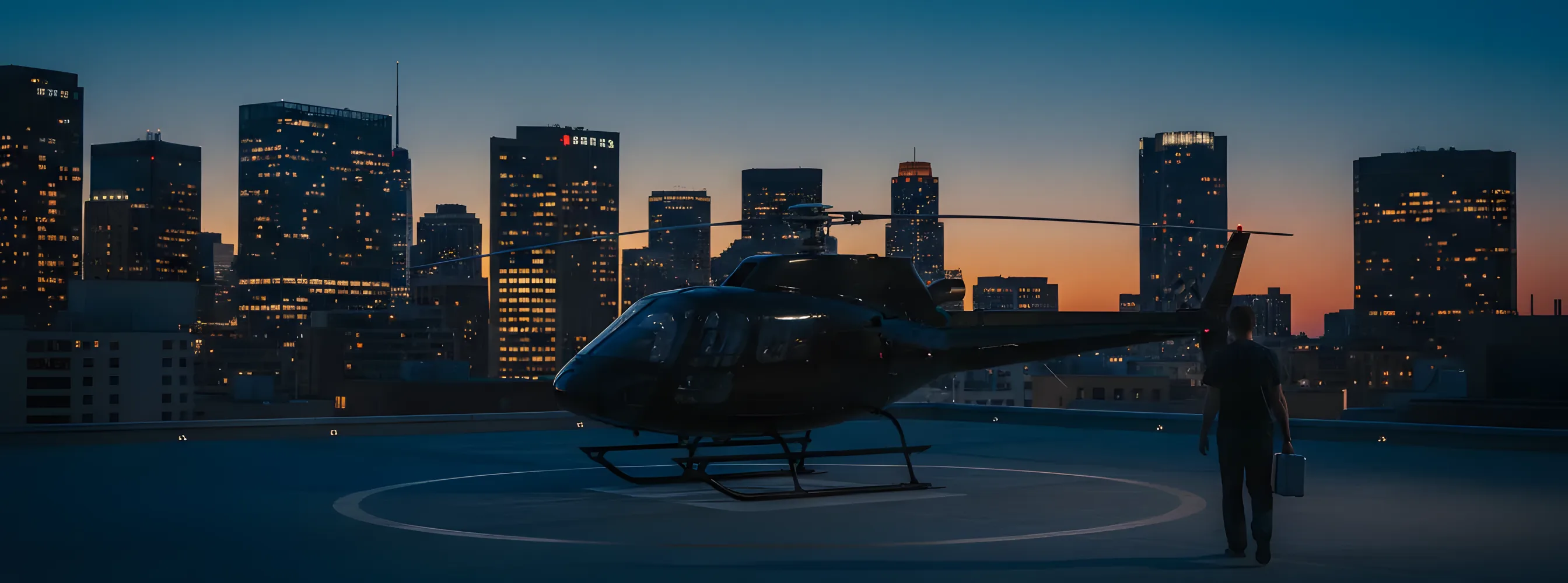 A helicopter on a hospital rooftop helipad at dusk, with a glowing city skyline in the background.
