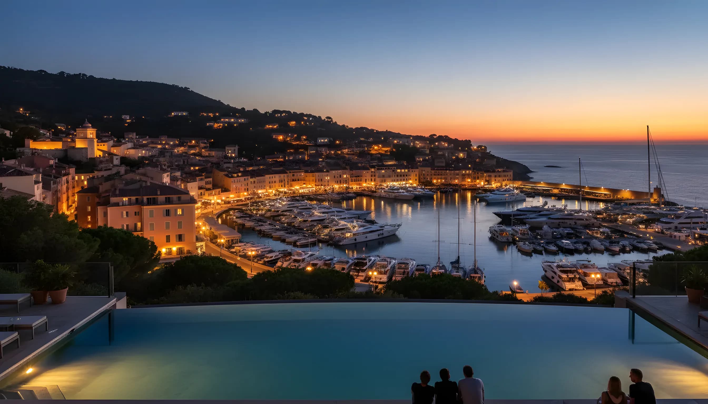 Panoramic view of the Port of Saint Tropez at dusk, with luxury yachts and illuminated town buildings.