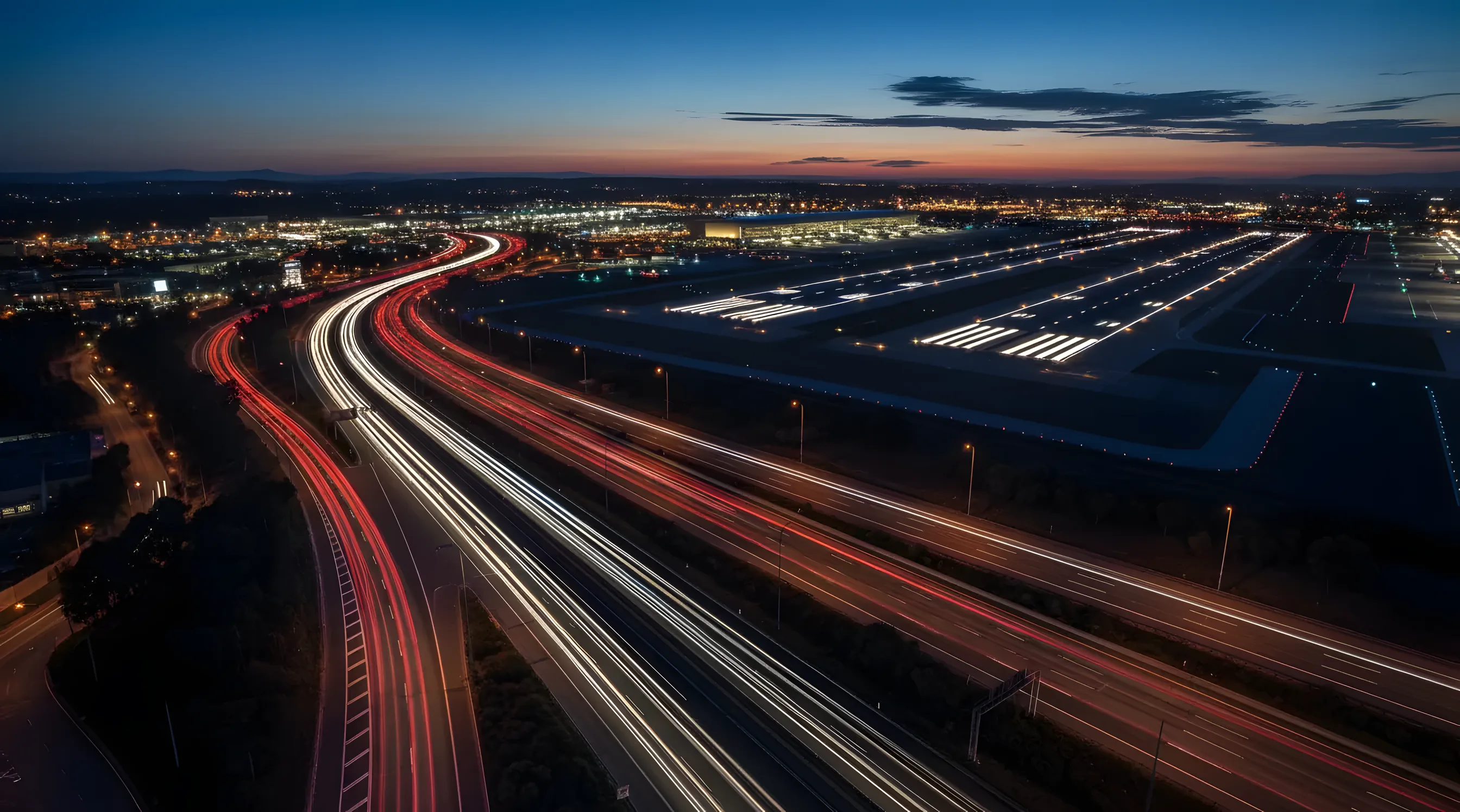 Light trails from cars on a highway leading towards a busy airport at dusk.