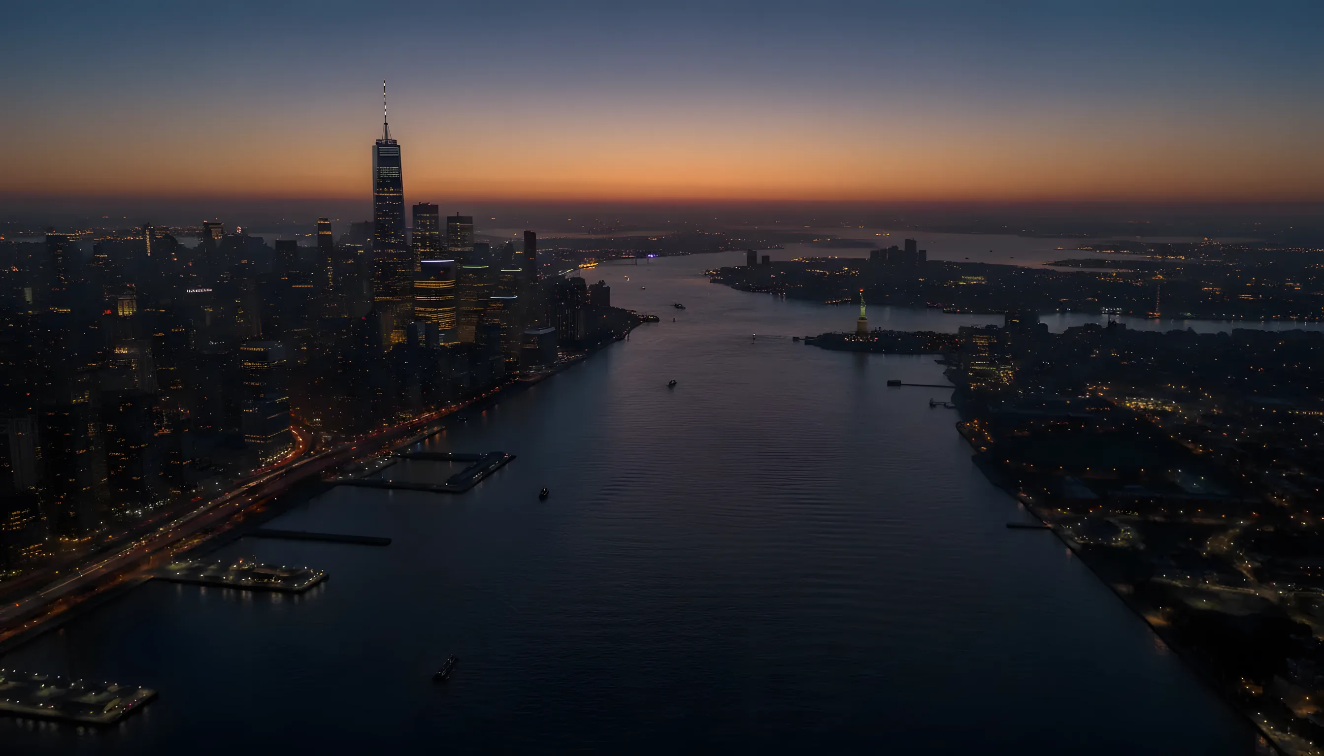 Aerial view of the Lower Manhattan skyline and the Statue of Liberty at dusk from across the Hudson River.
